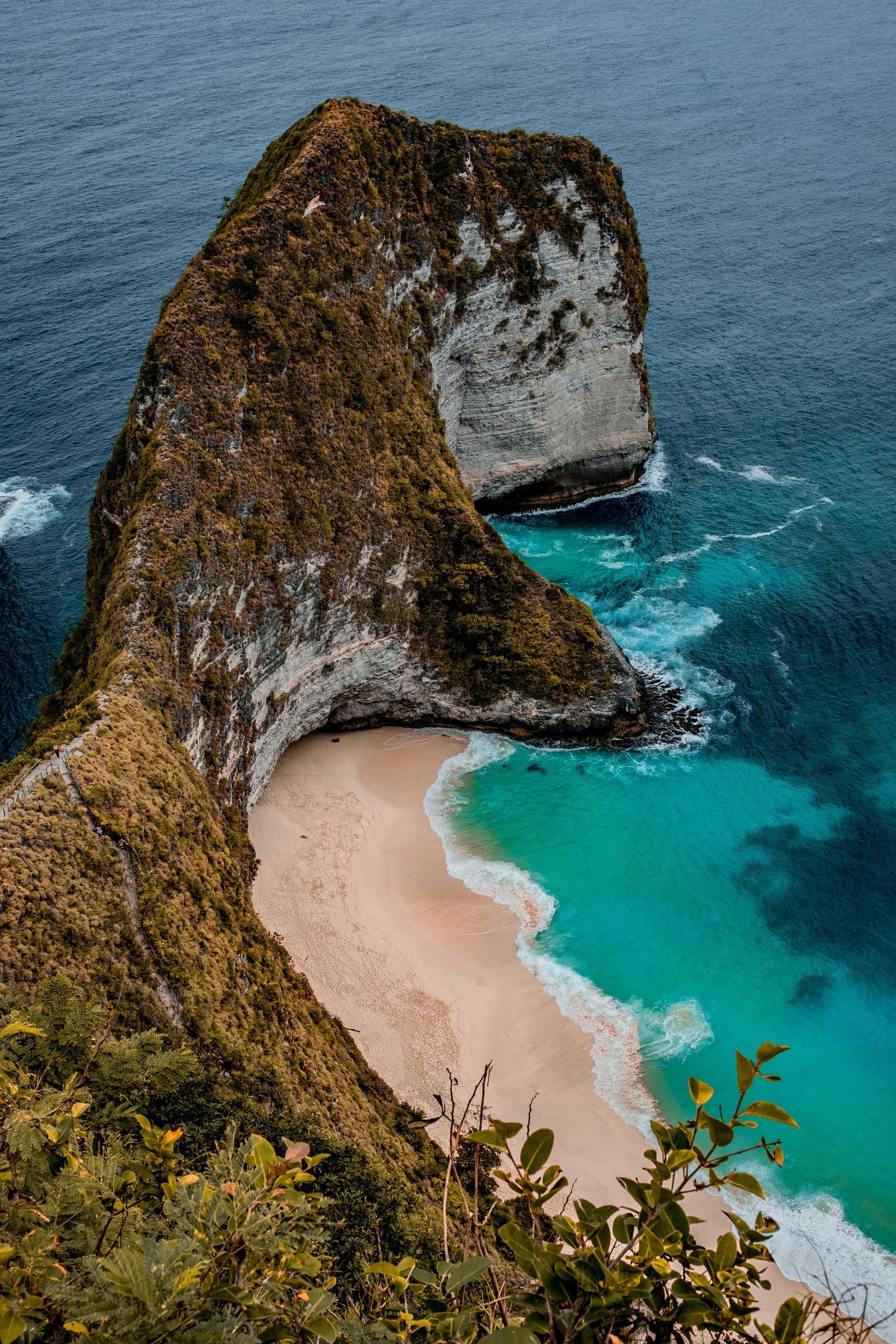 Rugged cliffside with a sandy beach and turquoise waters in Bali, Indonesia.