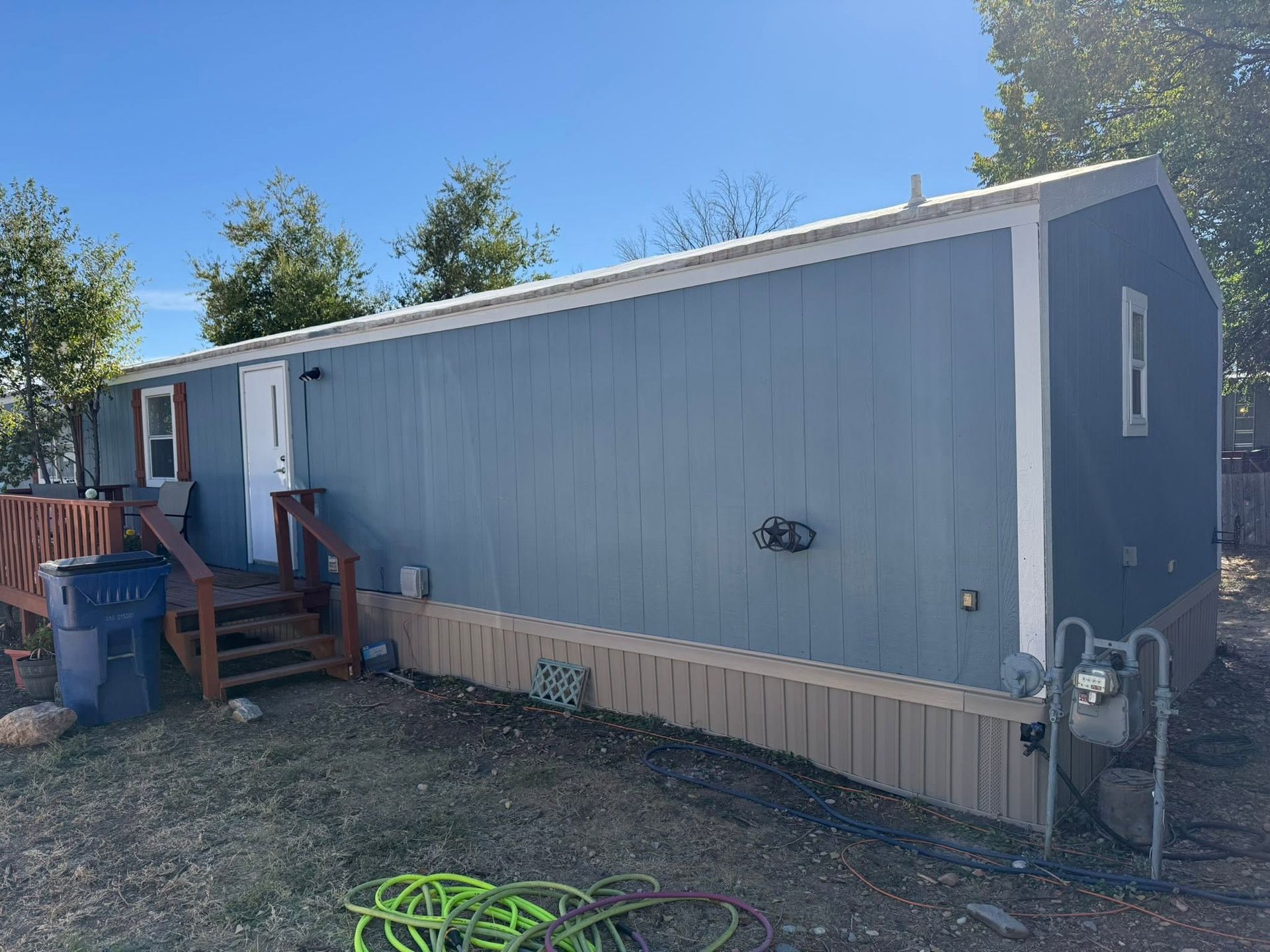 Blue mobile home with a small wooden porch and steps in a dry yard under a clear sky