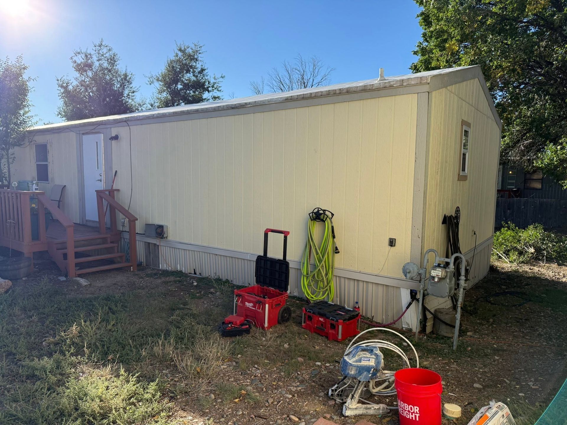 Mobile home exterior with red lawn equipment and a red bucket in the yard
