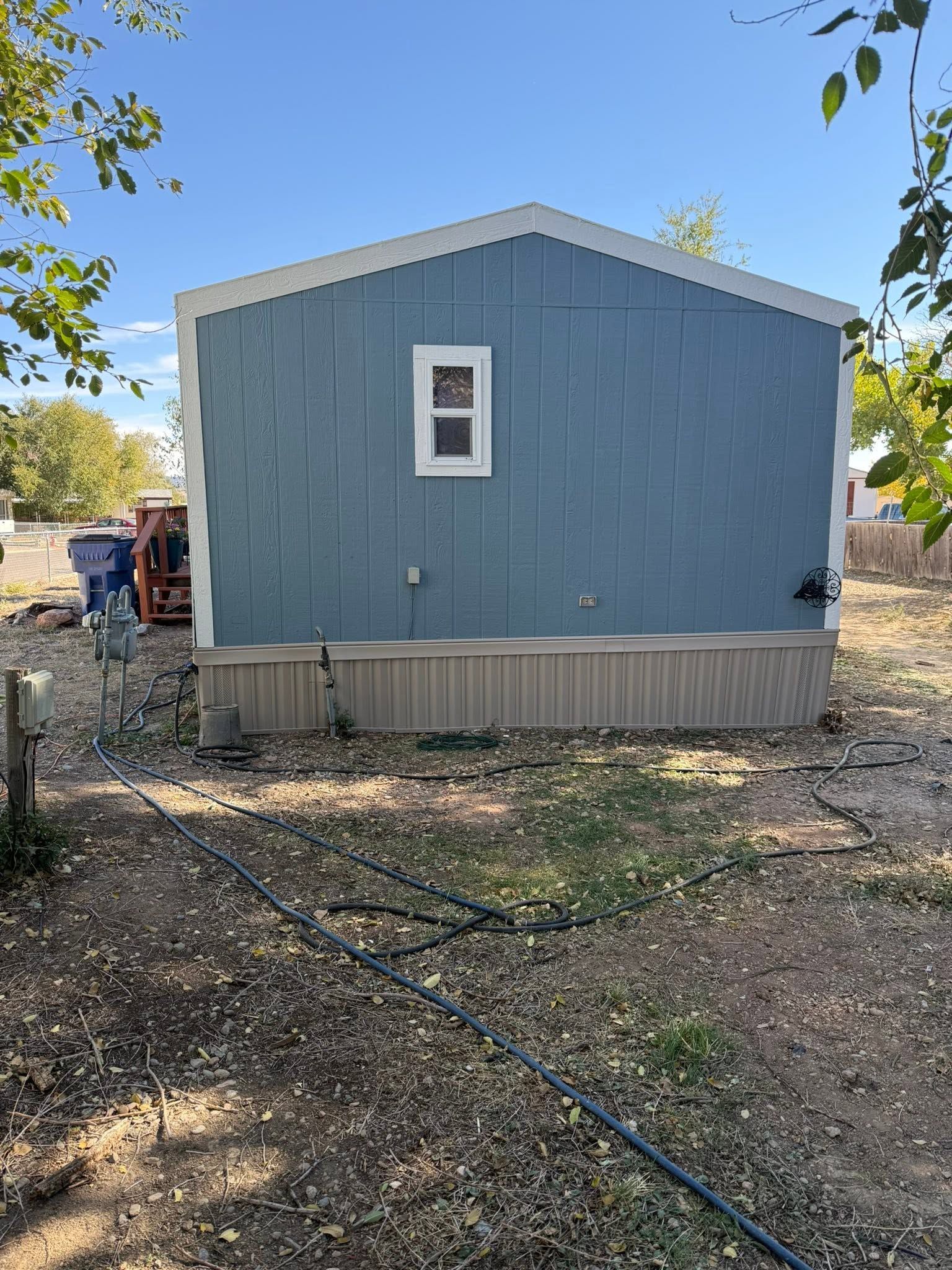 Blue shed with a small window and gray trim in a dry yard under a clear sky