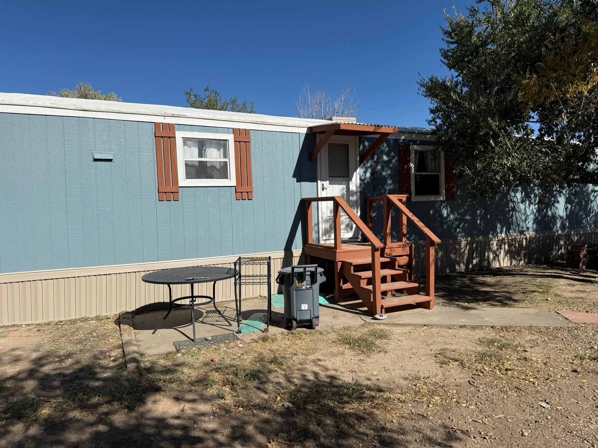 Blue mobile home with small wooden steps and porch in a dry yard under a clear sky