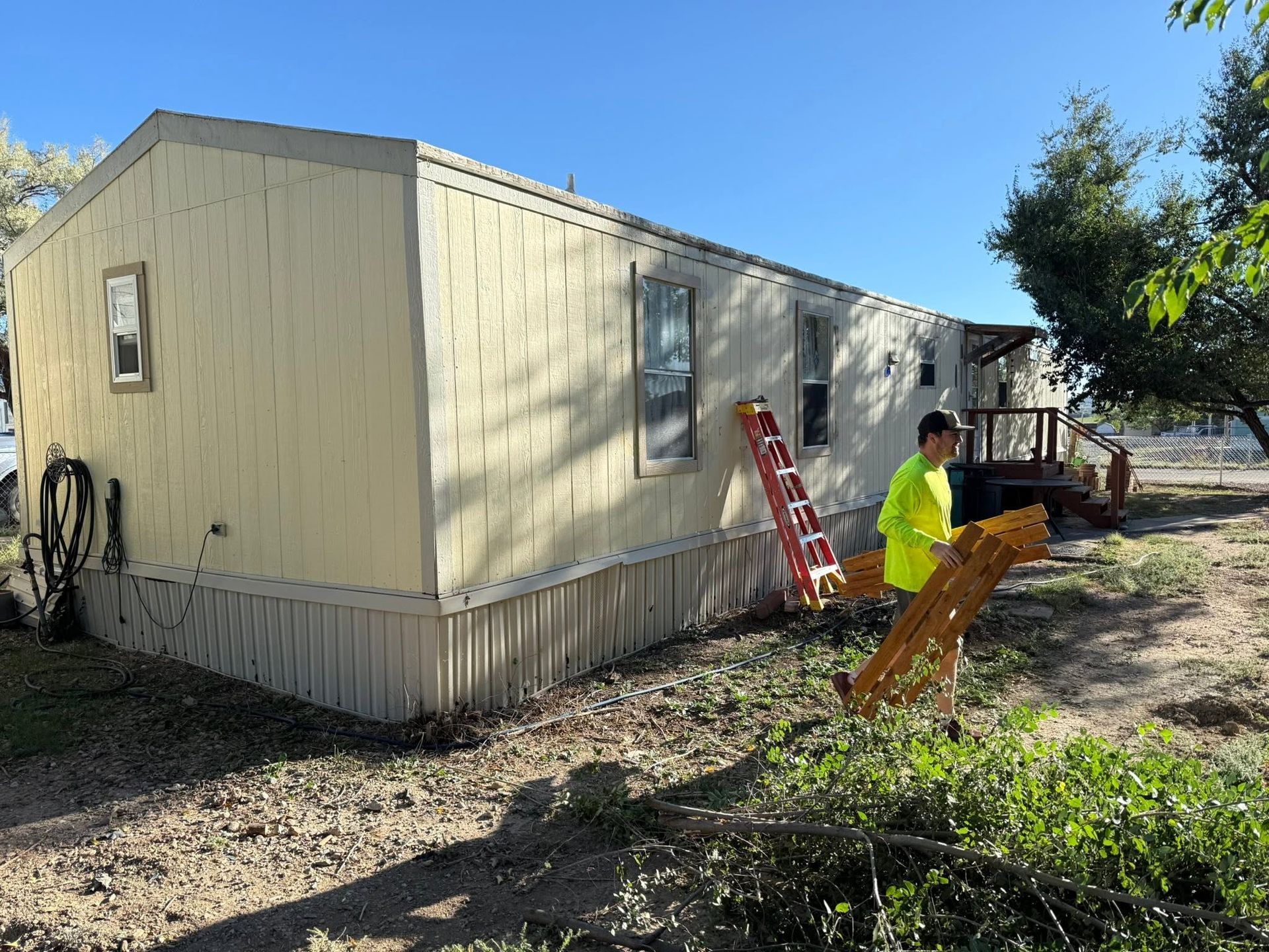 Workers repairing a beige mobile home with ladders and tools in a yard