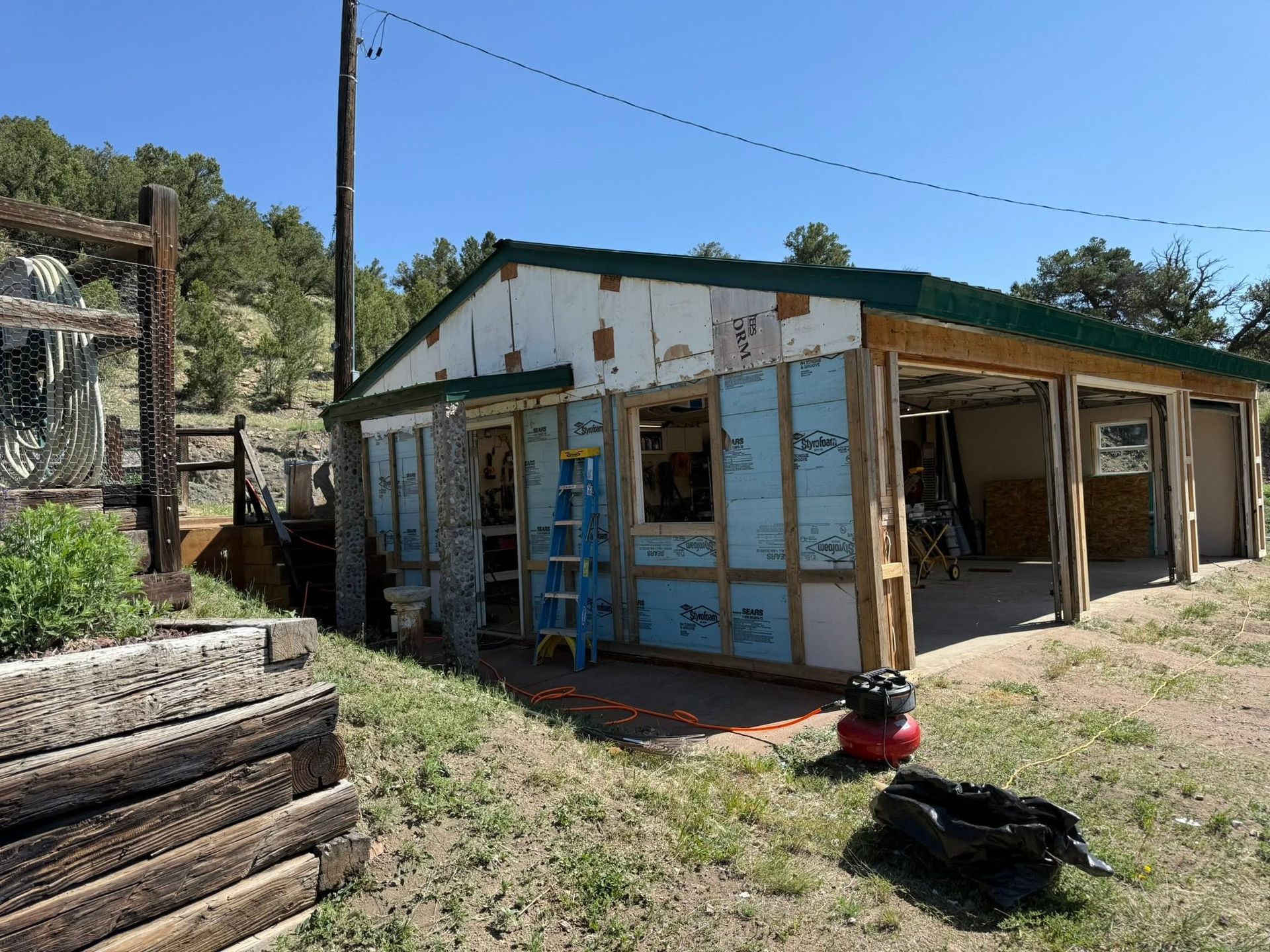 Weathered rural cabin with blue trim, open doorway, and ladder, surrounded by grass and trees.