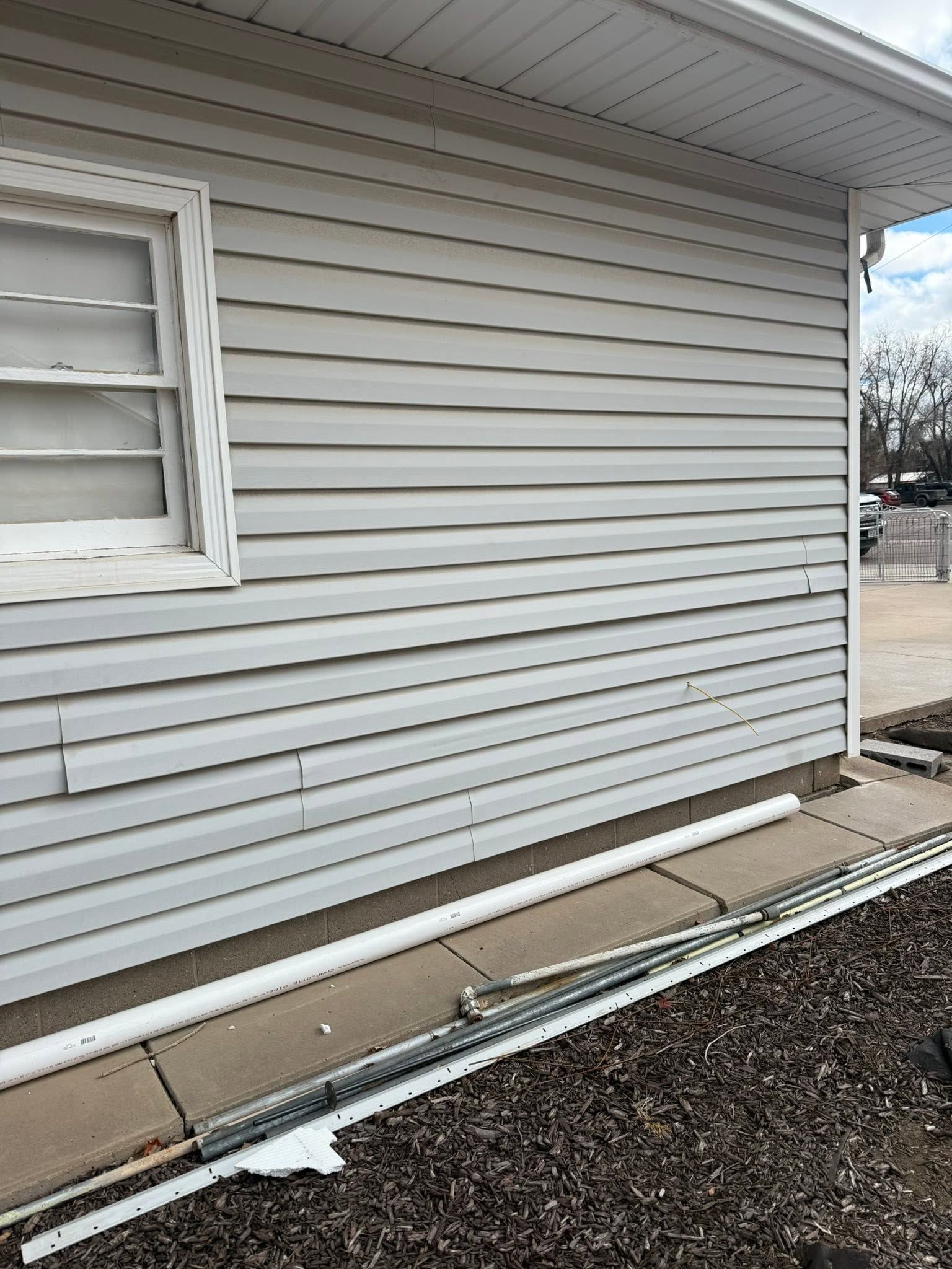 White vinyl-sided house exterior with a window and gravel border along the foundation