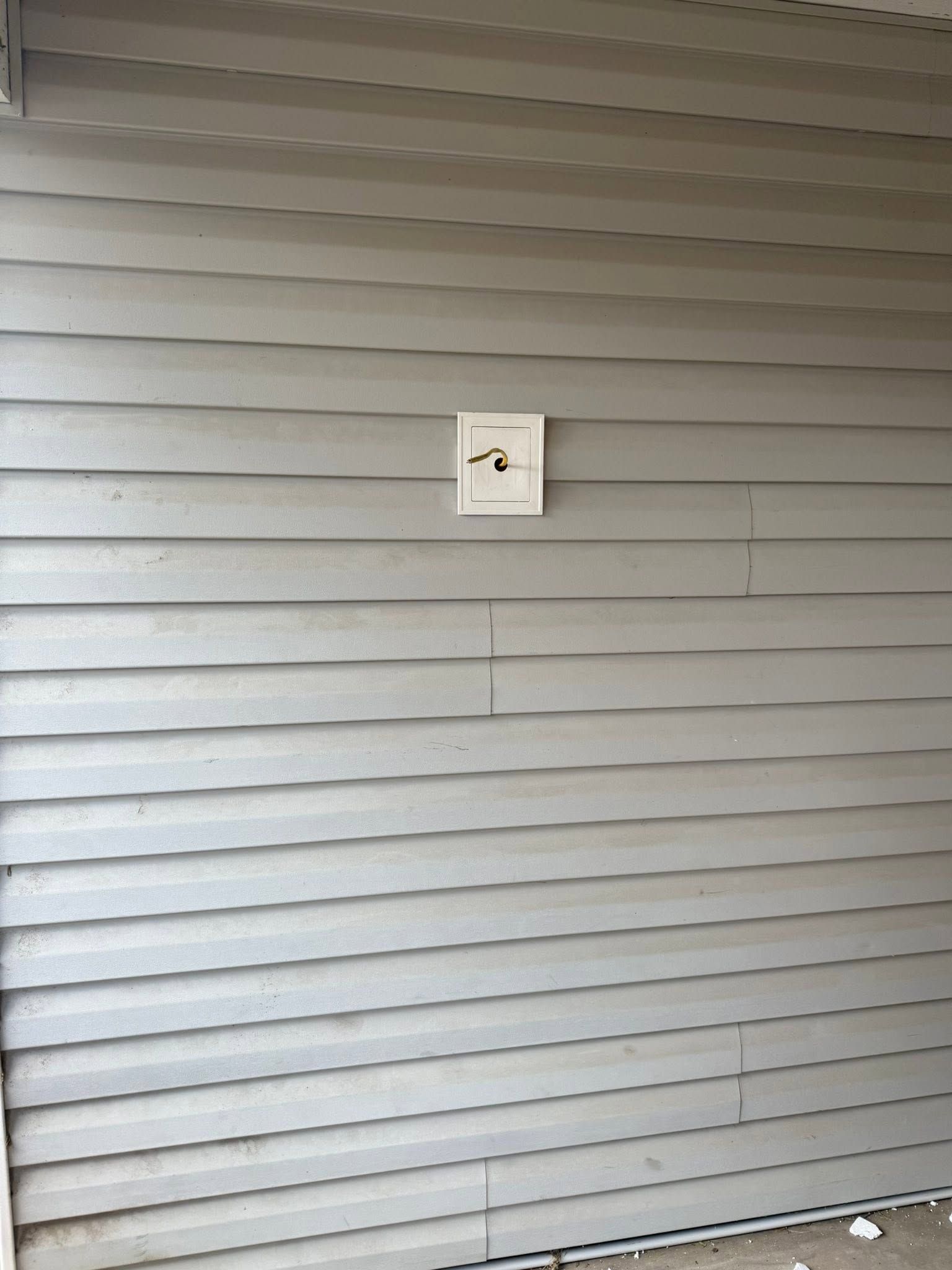 Gray vinyl siding wall with a small white square fixture centered on it.