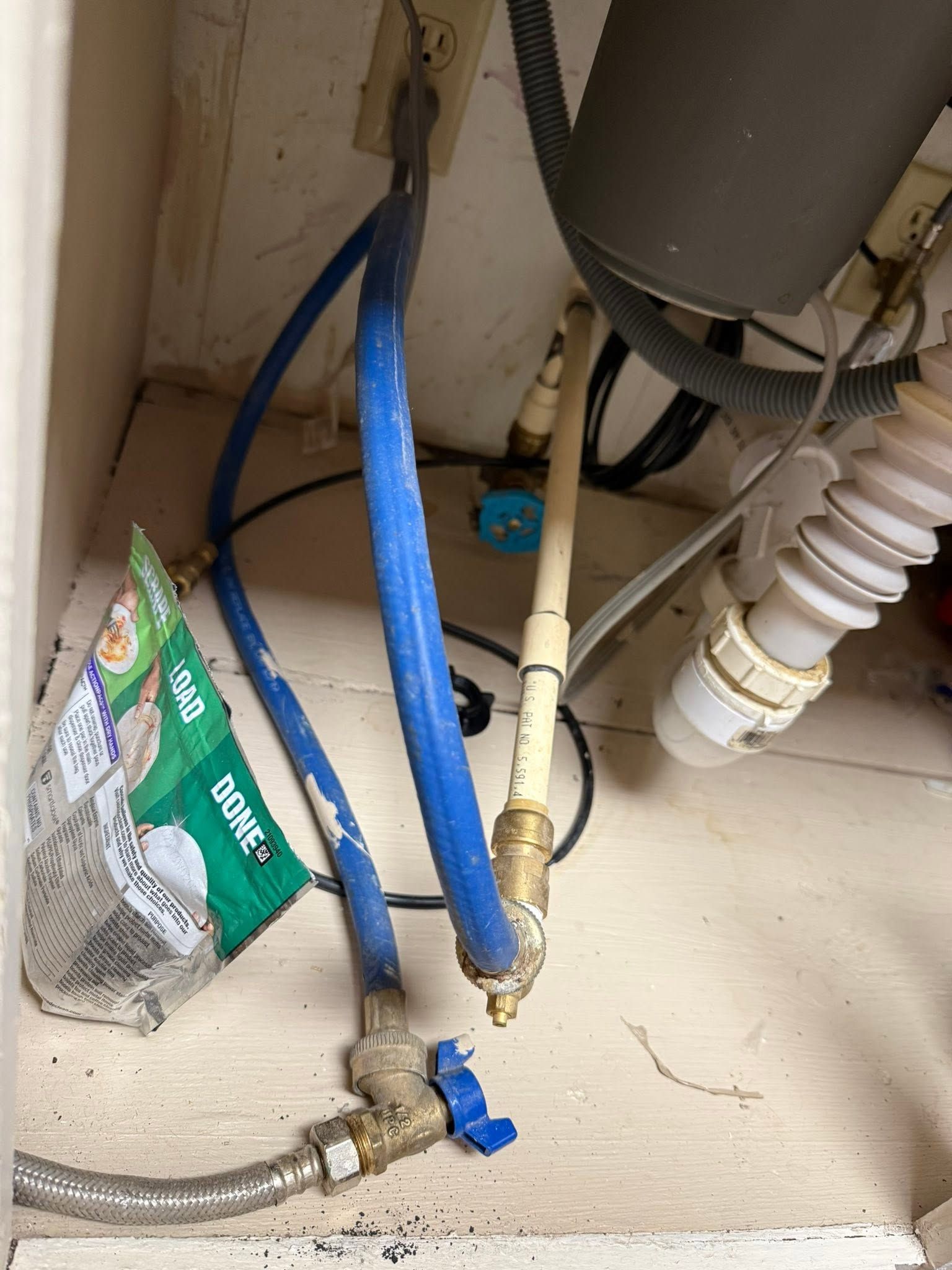Under-sink plumbing with blue and white hoses, valves, and a drain pipe in a cabinet.