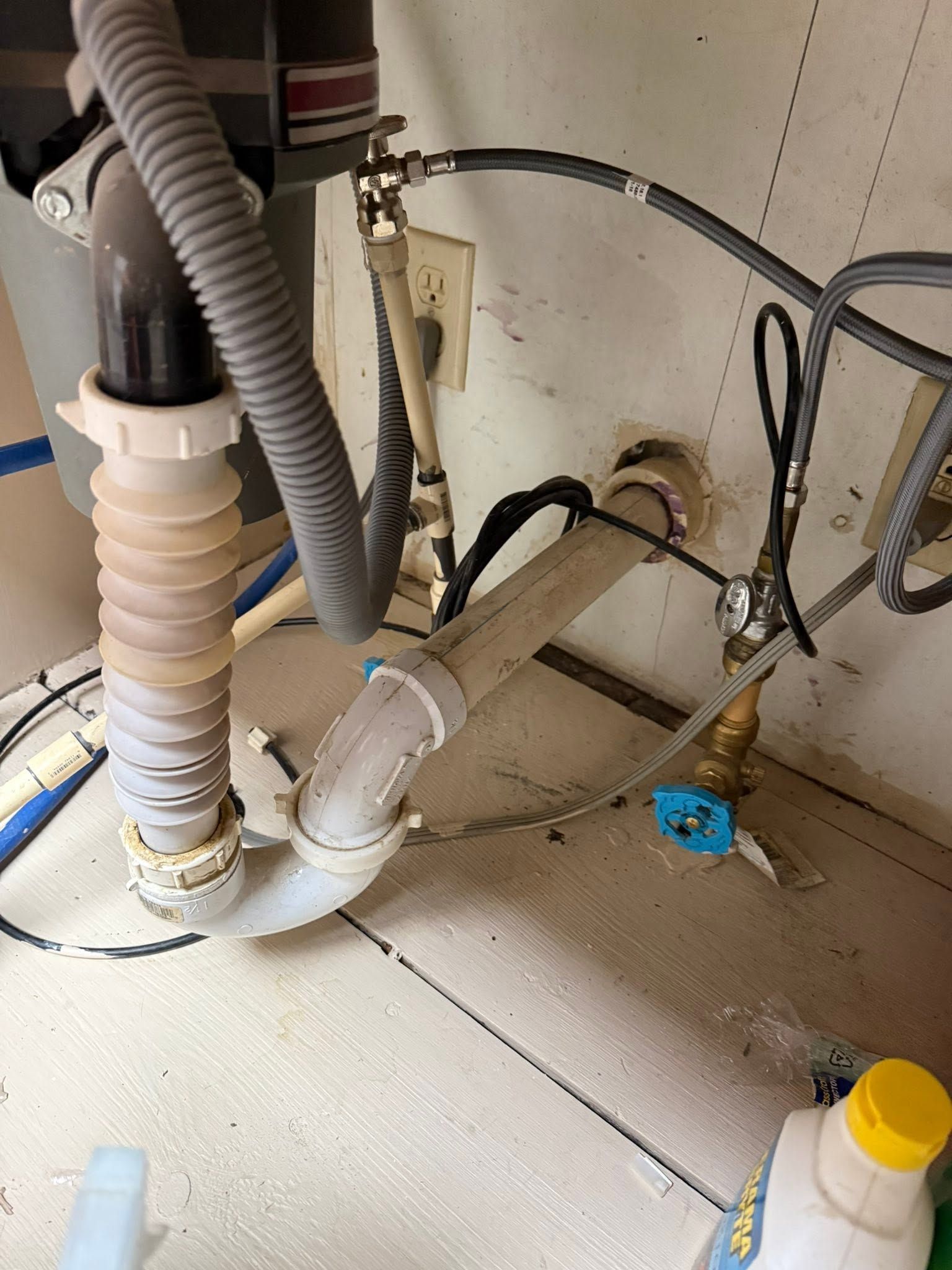 Under-sink plumbing and hoses with a blue shutoff valve on a tiled floor