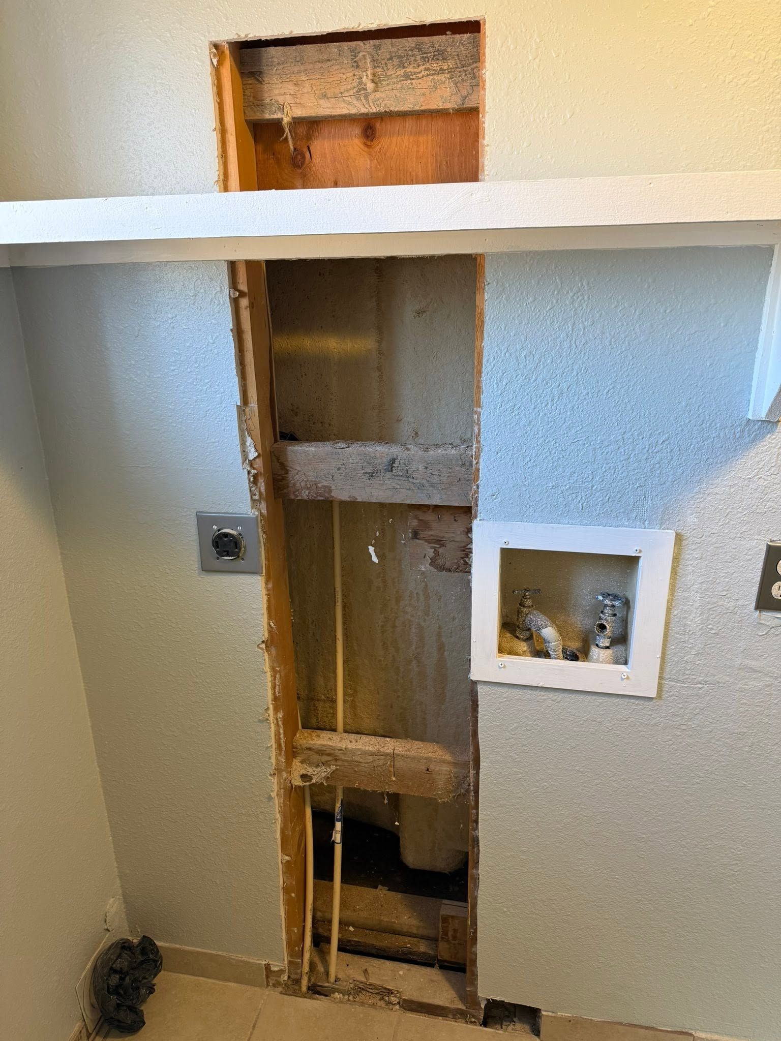 Open wall cavity in a room, with exposed wooden studs and drywall cutouts.