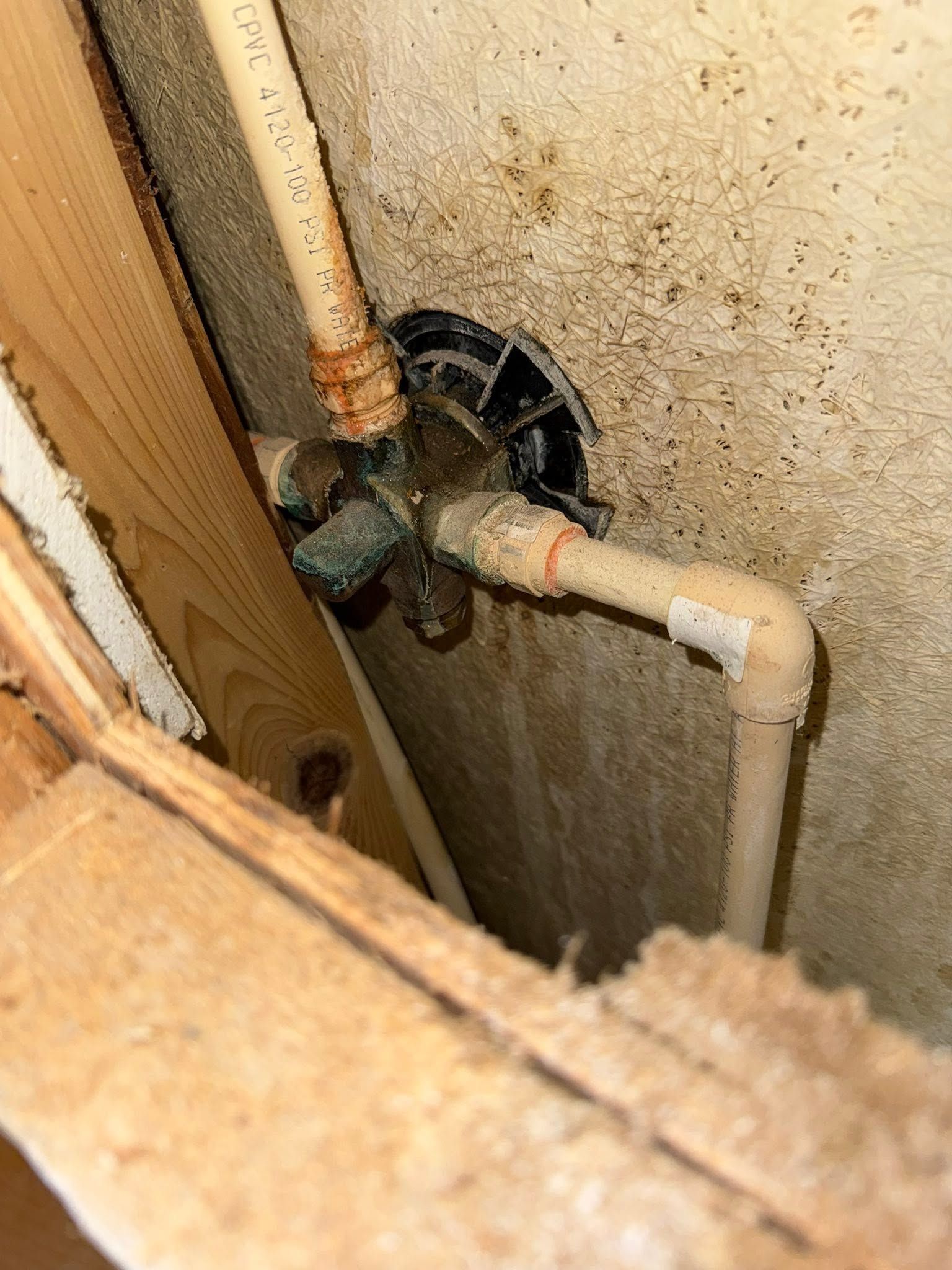 Plumbing pipes and a valve in a narrow wall cavity with water stains and mold on the wall