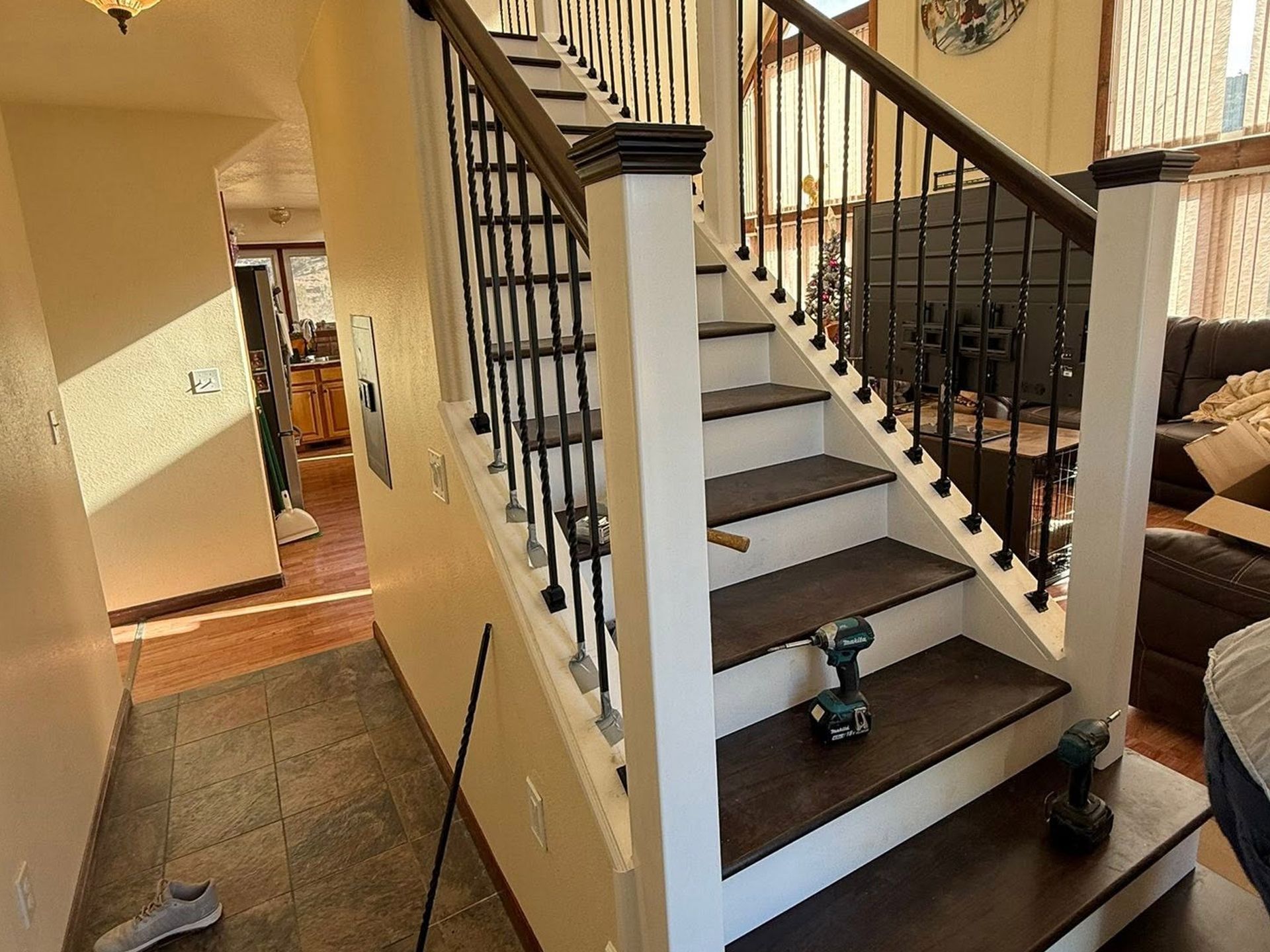 Staircase with dark railings in a sunlit home hallway, with a power drill on the steps.