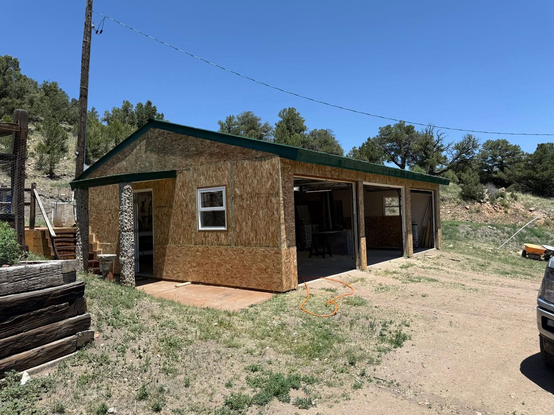 Small tan wooden shed with a green roof on a dirt lot under a clear blue sky.