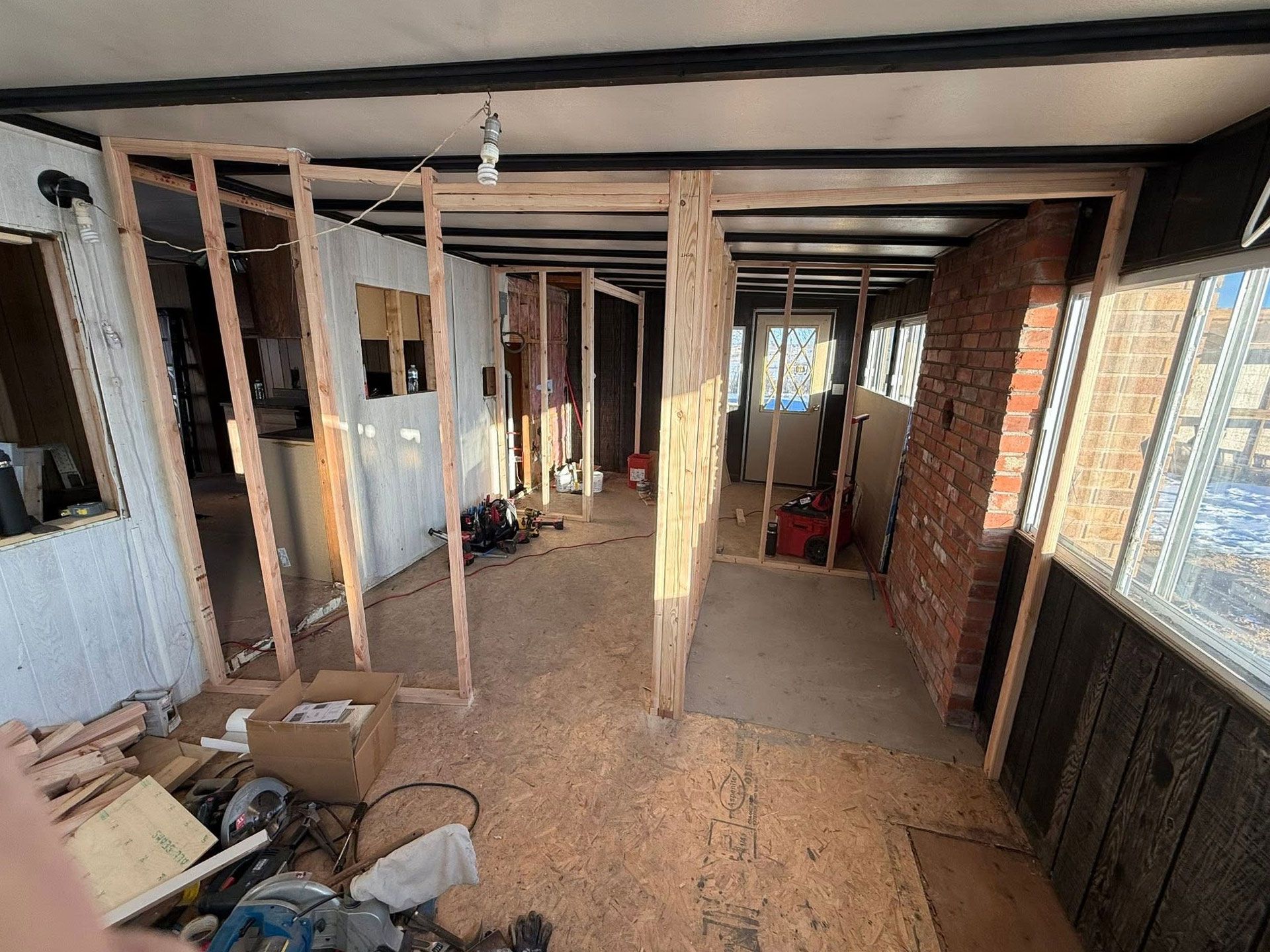Interior of a house under renovation with exposed studs, debris, and large windows on the right