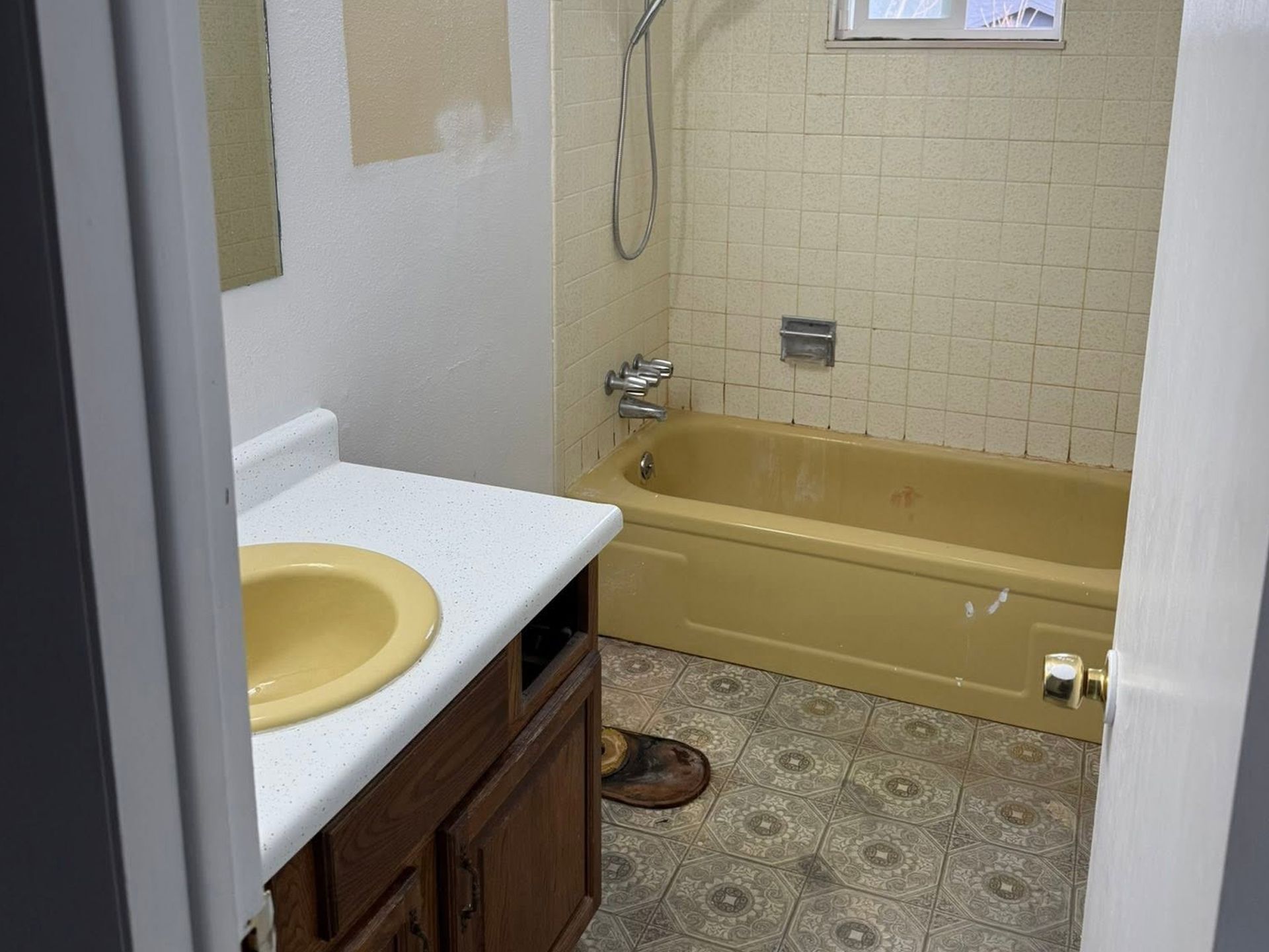 Small bathroom with yellow tub, tiled wall, and brown vanity with a white countertop.