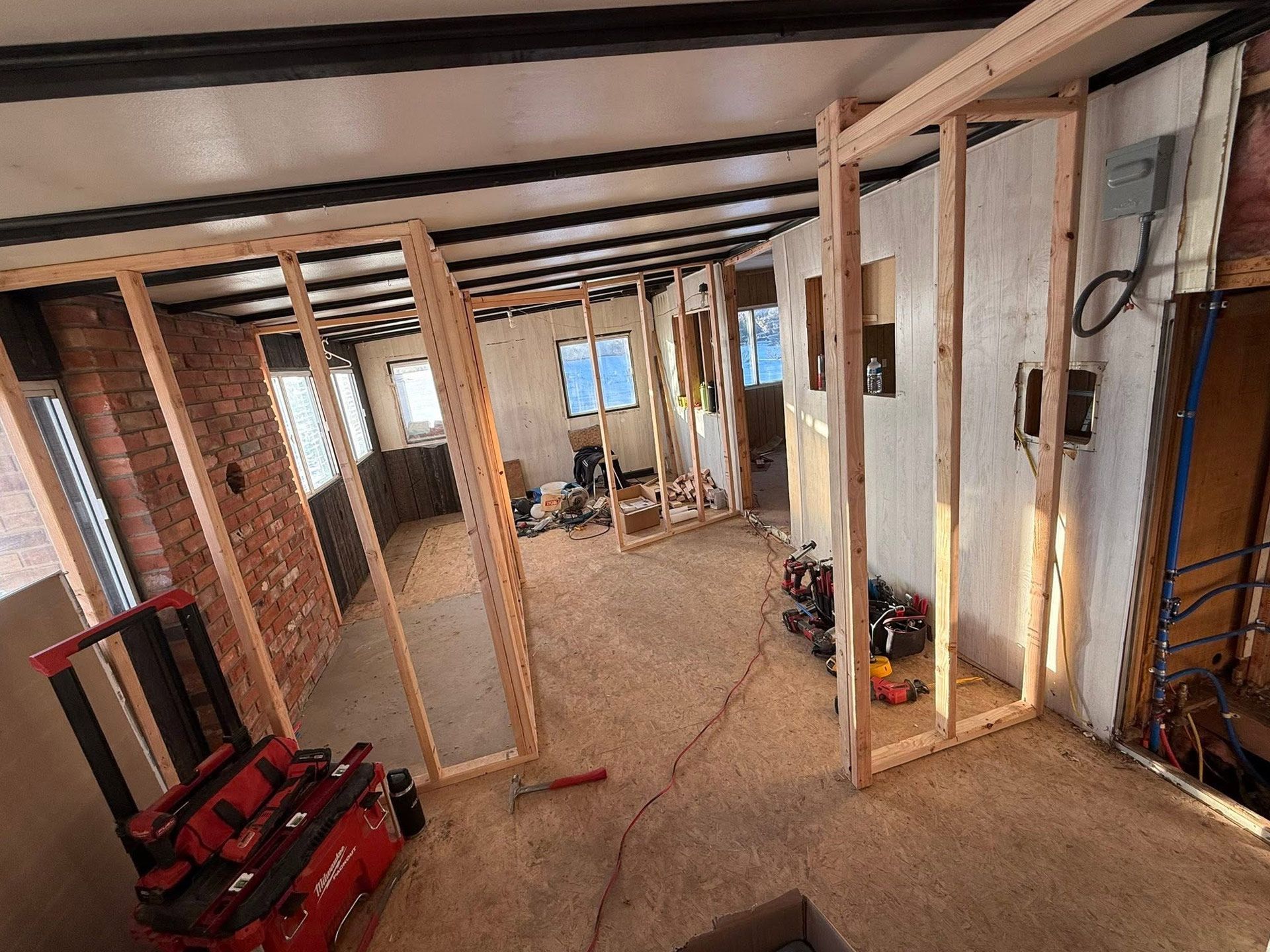 Partially framed basement interior with exposed beams, brick walls, and construction tools on the floor