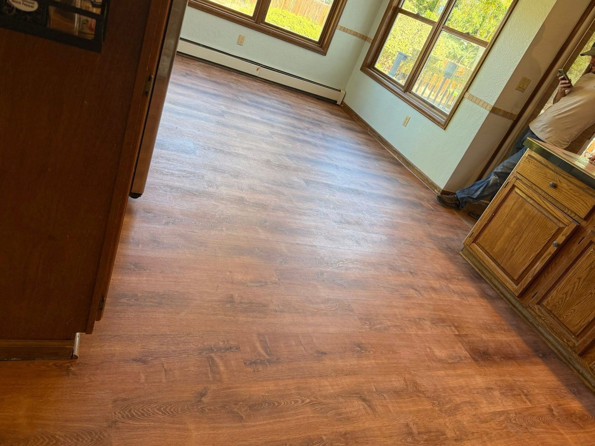 Empty room with wood flooring, windows, and a wooden cabinet on the right.