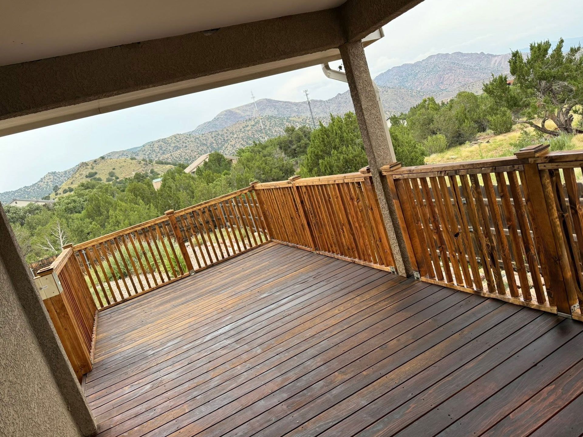 Wooden deck with railings overlooking green hills and mountains under a covered patio