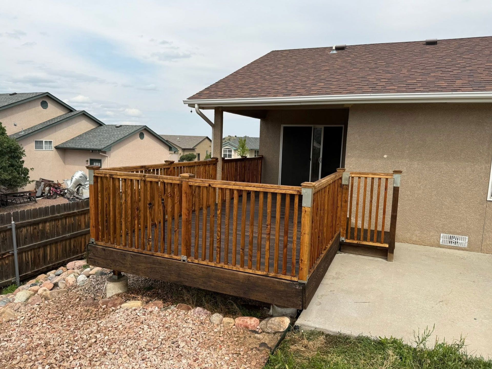 Backyard wooden deck with railing beside a stucco house and concrete patio