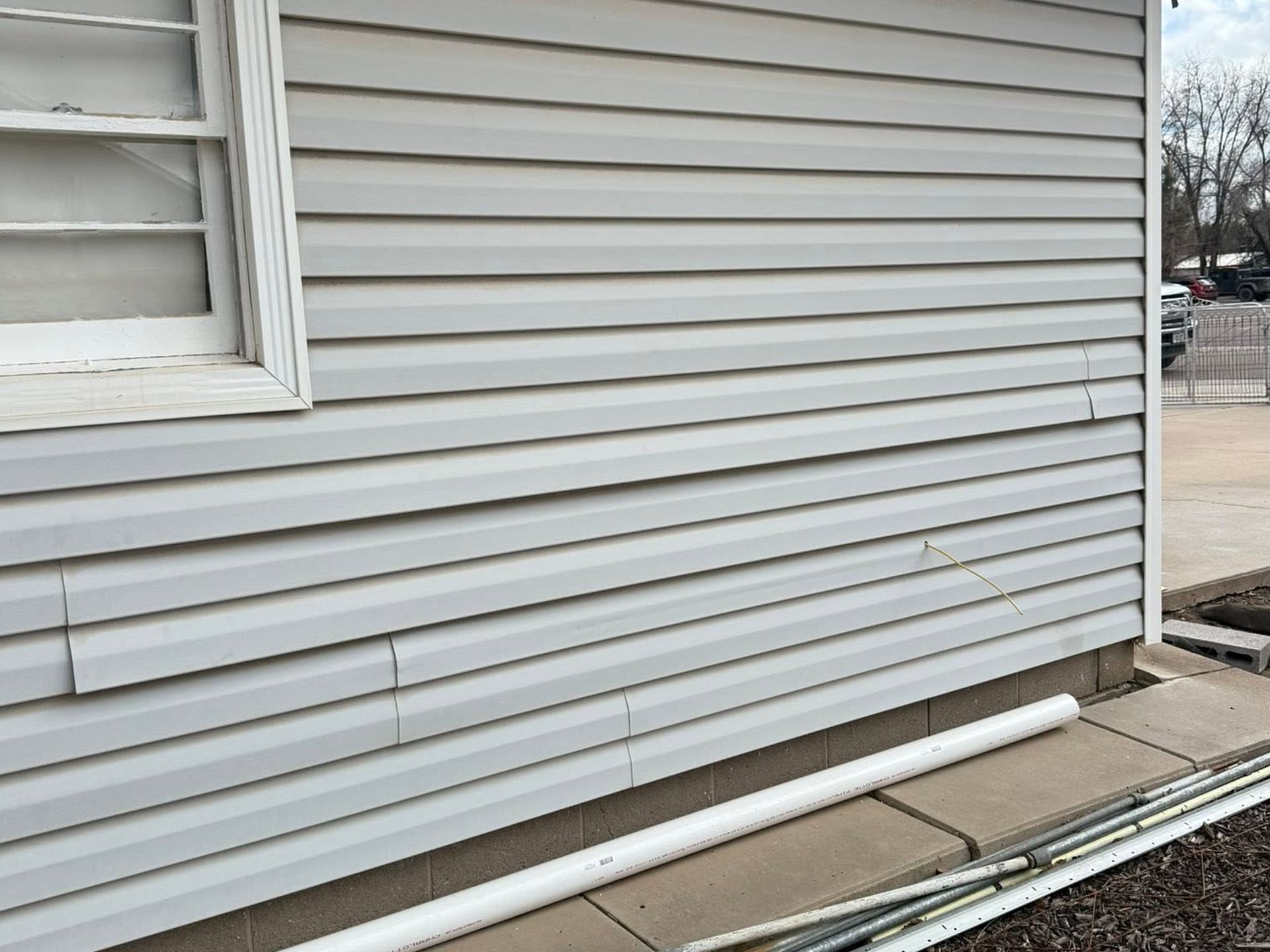 Gray house siding with a white downspout along a paved walkway beside a snow-lined street