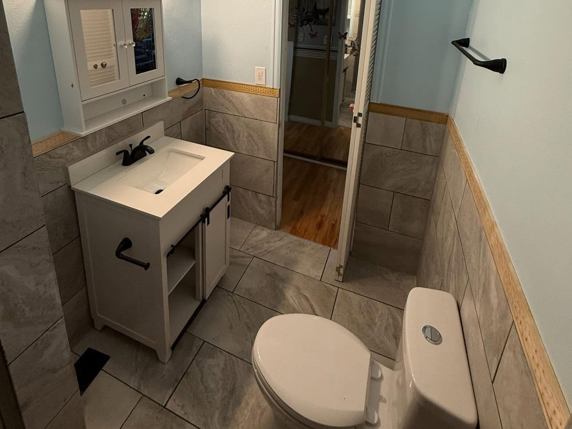 Small bathroom with sink, toilet, tiled floor, mirror, and an open door to a hallway.