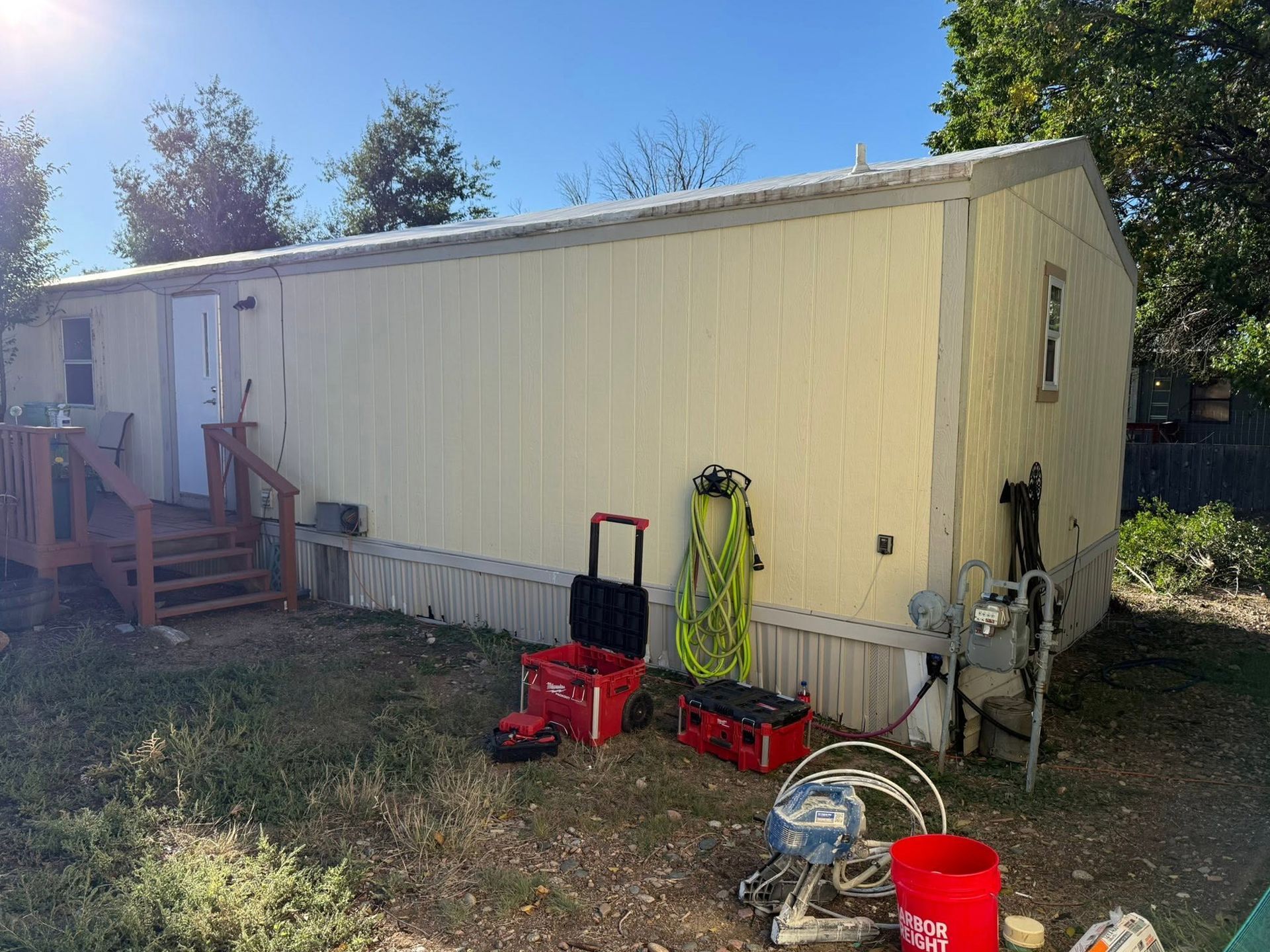 Yellow mobile home exterior with tools and buckets in a grassy yard