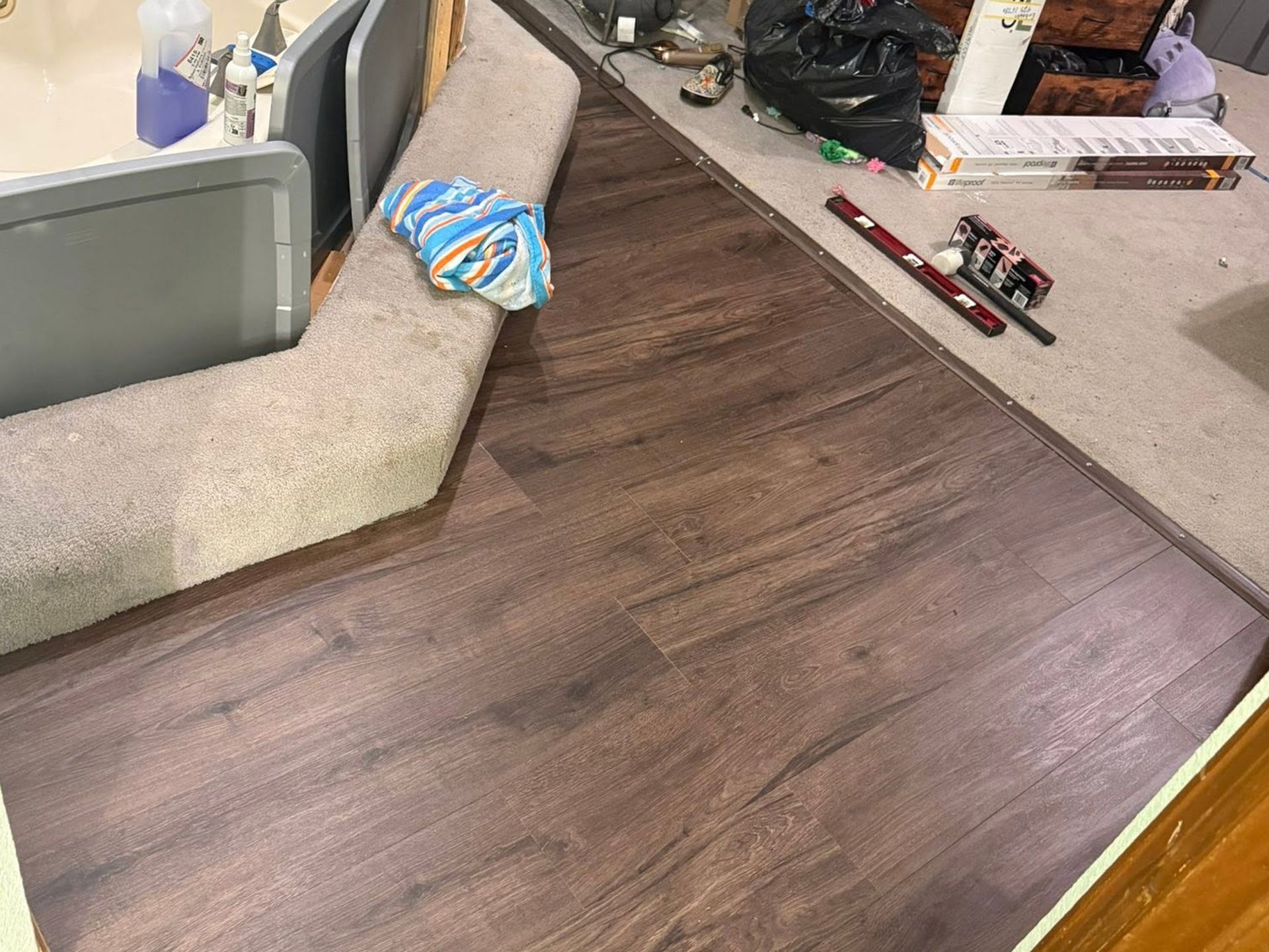 Wood-look flooring sample beside a carpeted sofa and countertop with small toy vehicles.