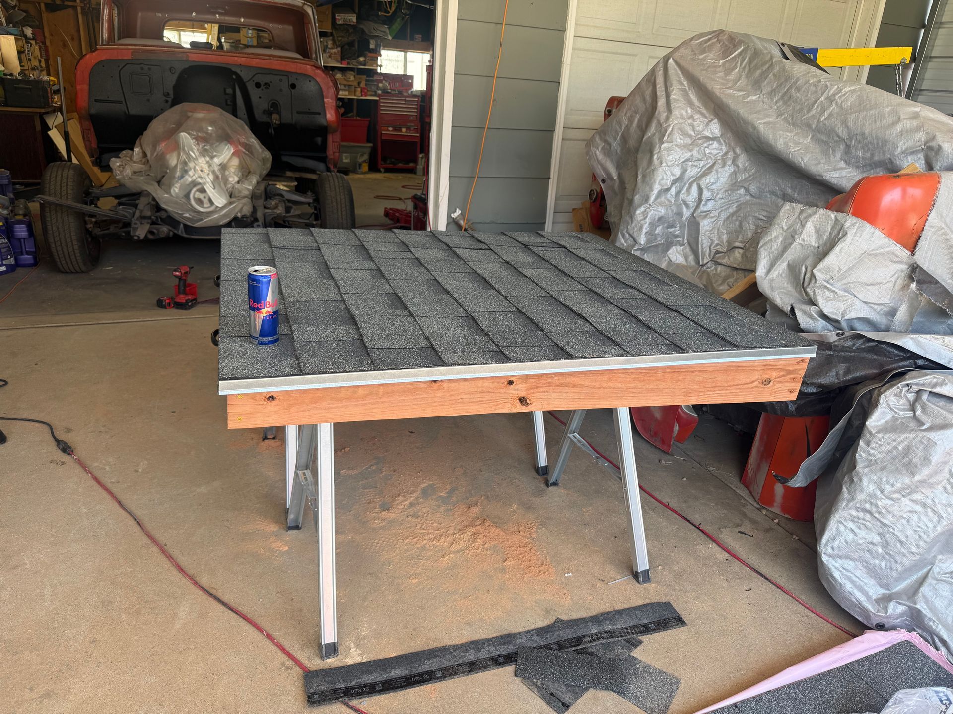 Small work table with gray textured surface in a cluttered garage, with a soda can on top.