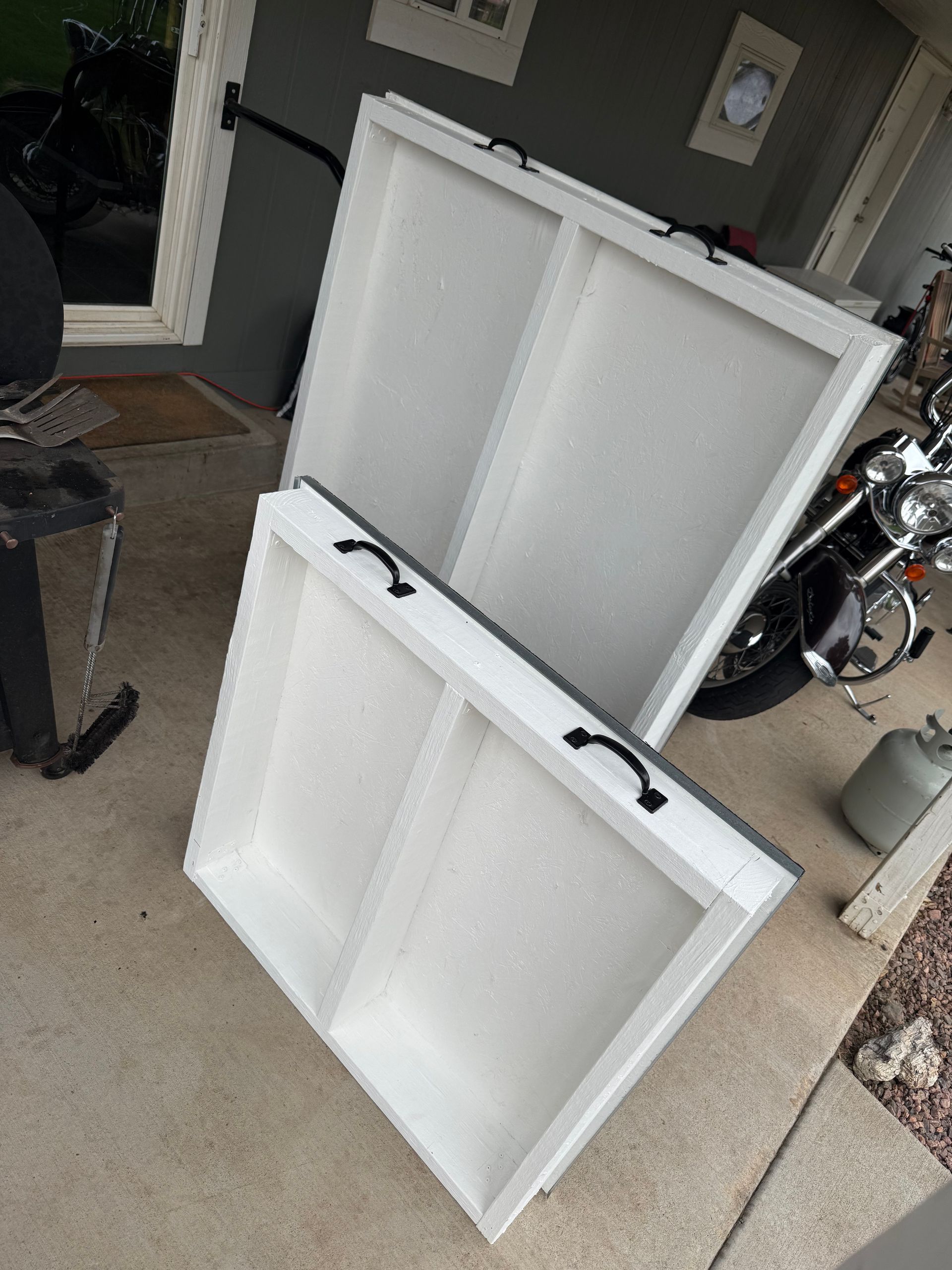 Two white folding tables leaned together on a garage floor, with a motorcycle in the background.