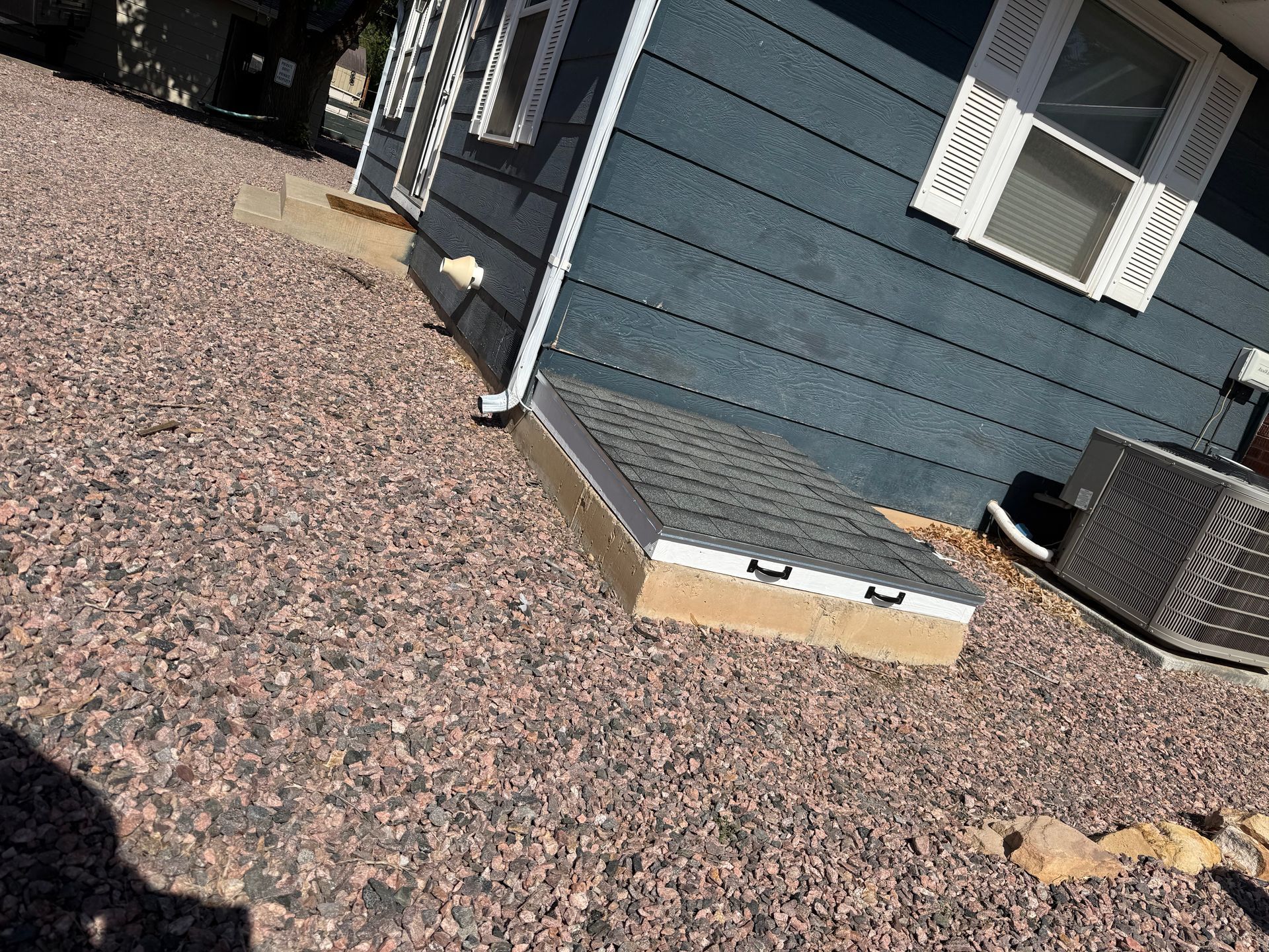 Blue house exterior with white shutters and gravel yard beside an AC unit