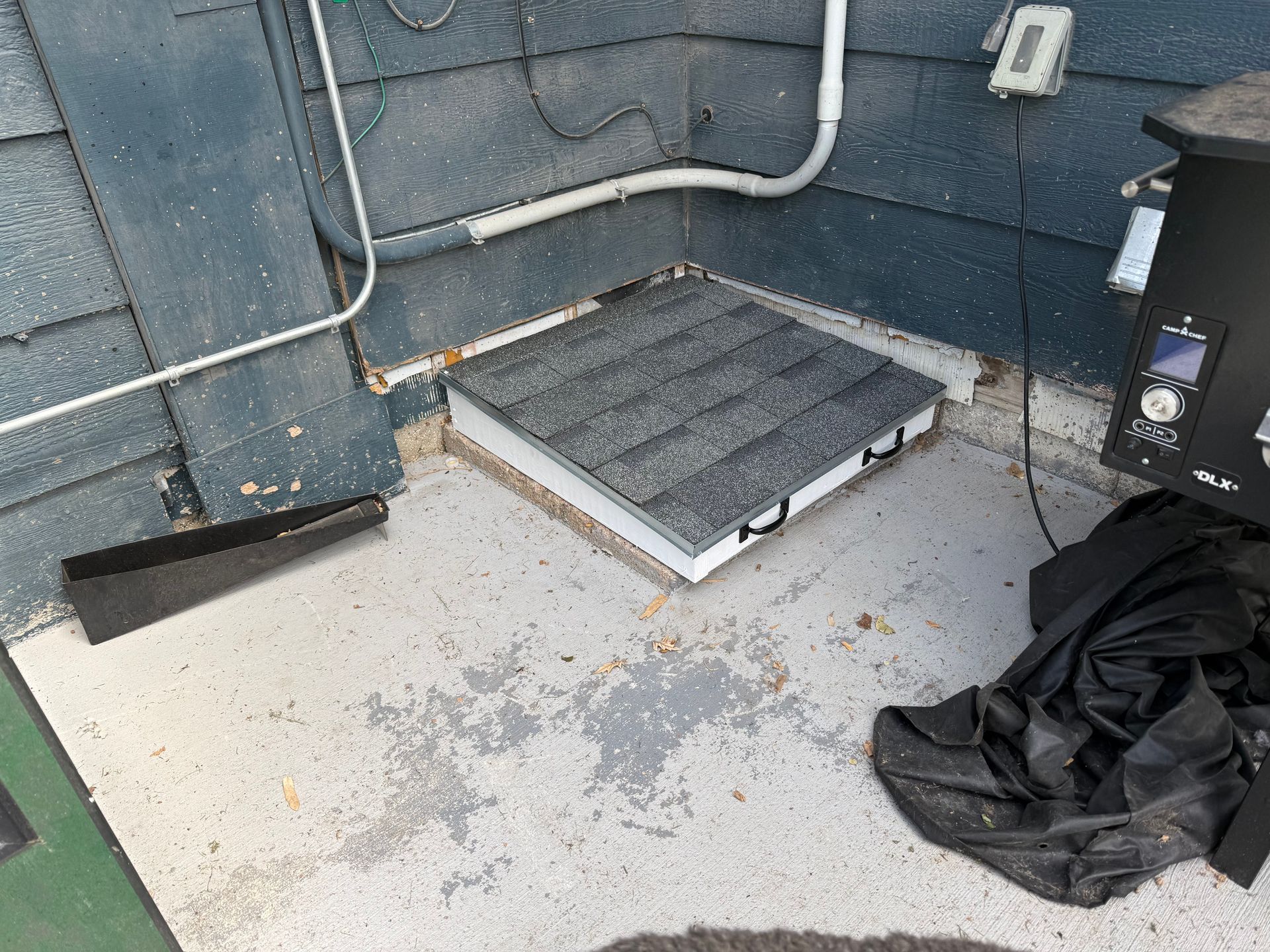 Rooftop utility area with gray floor, metal pipes, a black vent unit, and a pile of black trash bags.