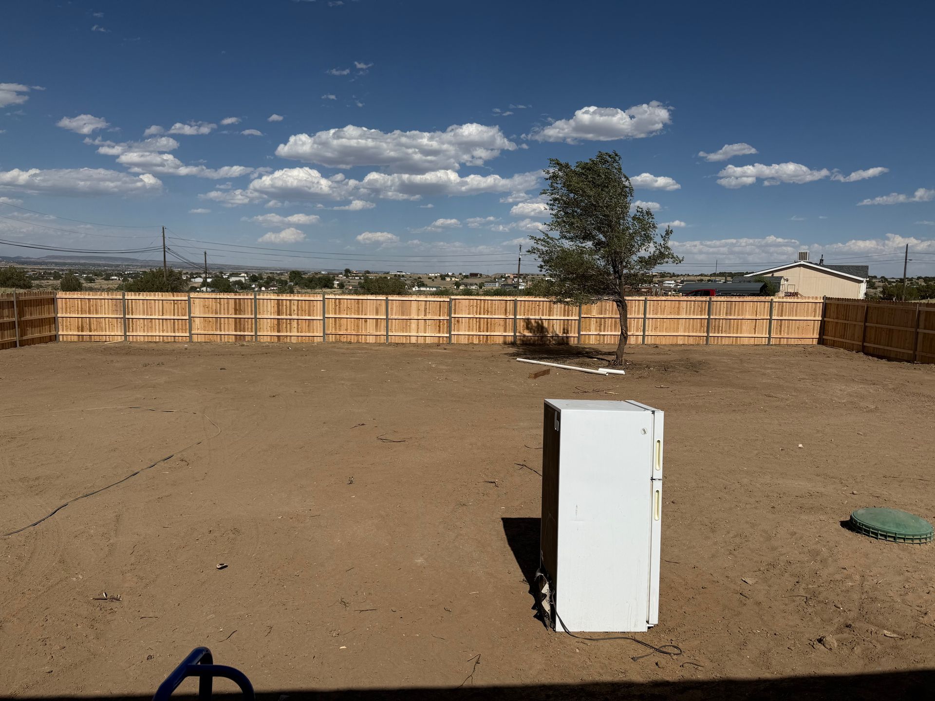 White appliance standing alone in a dusty yard with a wooden fence and blue sky in the background