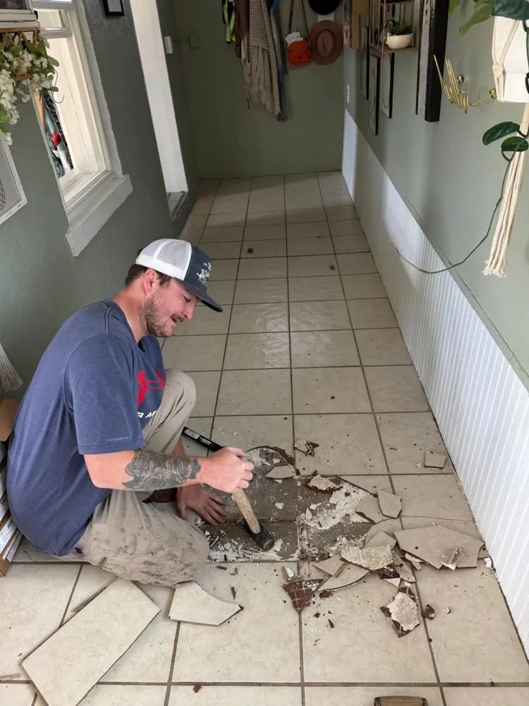 Worker removing broken floor tiles in a narrow hallway