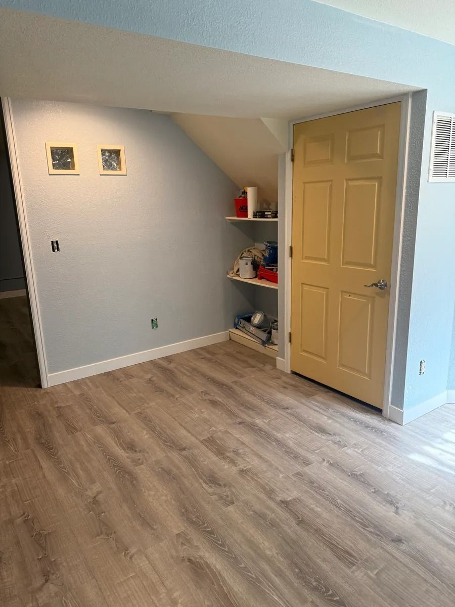 Empty room with light wood flooring, beige walls, a closet nook with shelves, and an open tan door.