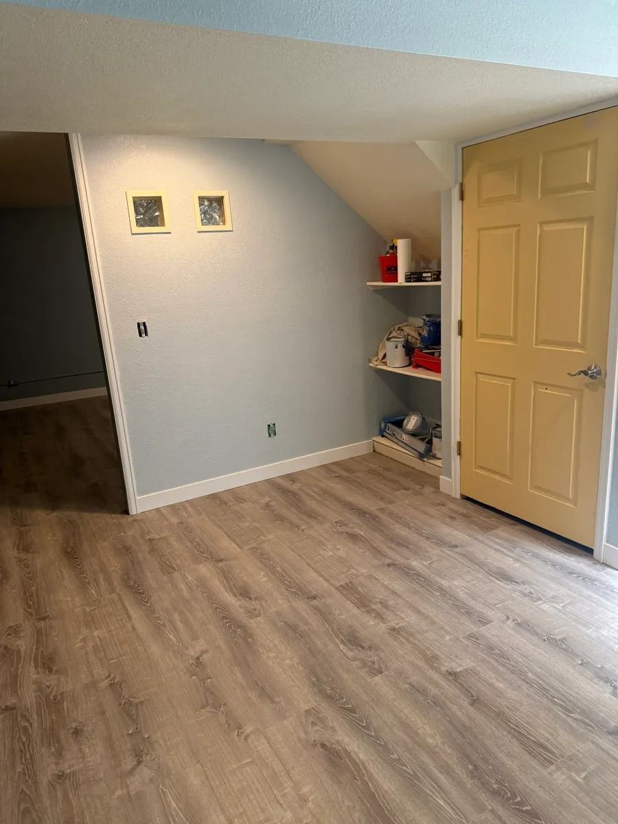 Empty room with light wood flooring, gray walls, a closet door, and small corner shelves.
