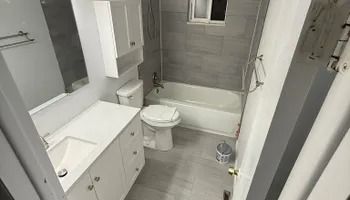 Small modern bathroom with white tub, toilet, sink vanity, and gray tile flooring.