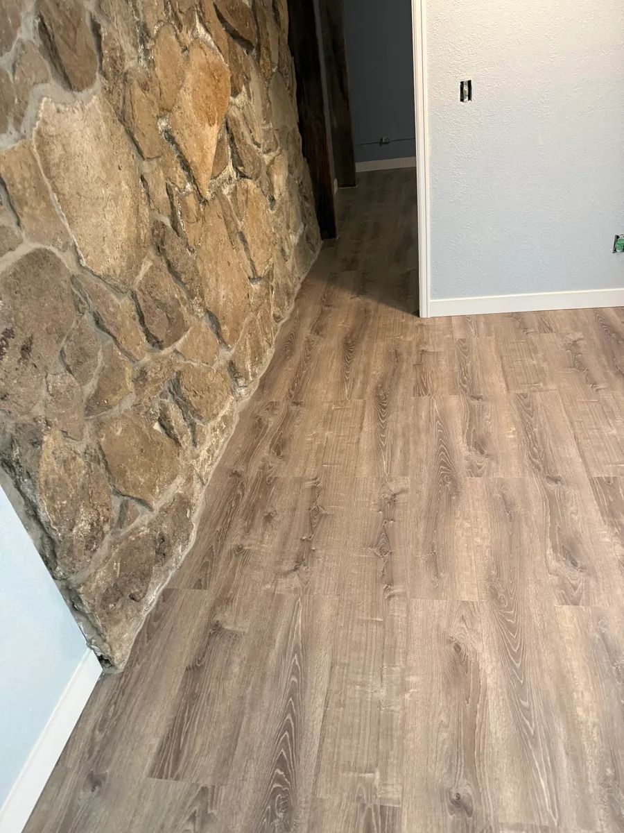 Stone wall and light wood flooring in a narrow hallway with a white doorway.