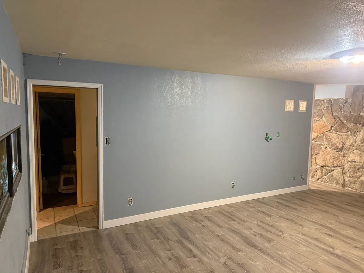 Empty living room with gray walls, wood-look floor, and stone accent wall by an open doorway