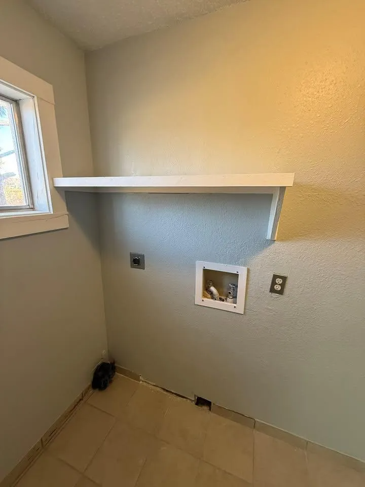 Empty laundry room with a window, white shelf, hookups, and tile floor