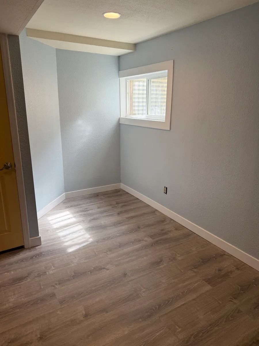 Empty light gray room with wood-look flooring, small window, and sunlight on the floor