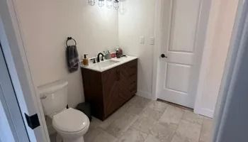 Small bathroom with a toilet, dark wood vanity, white sink, and tiled floor.