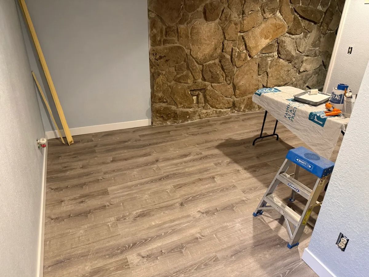 Empty room with wood-look flooring, stone accent wall, and a folding table with supplies on the right.