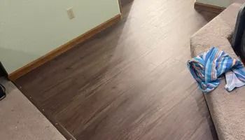 Empty room with dark wood flooring, beige walls, and a blue striped cloth on the right side of a couch