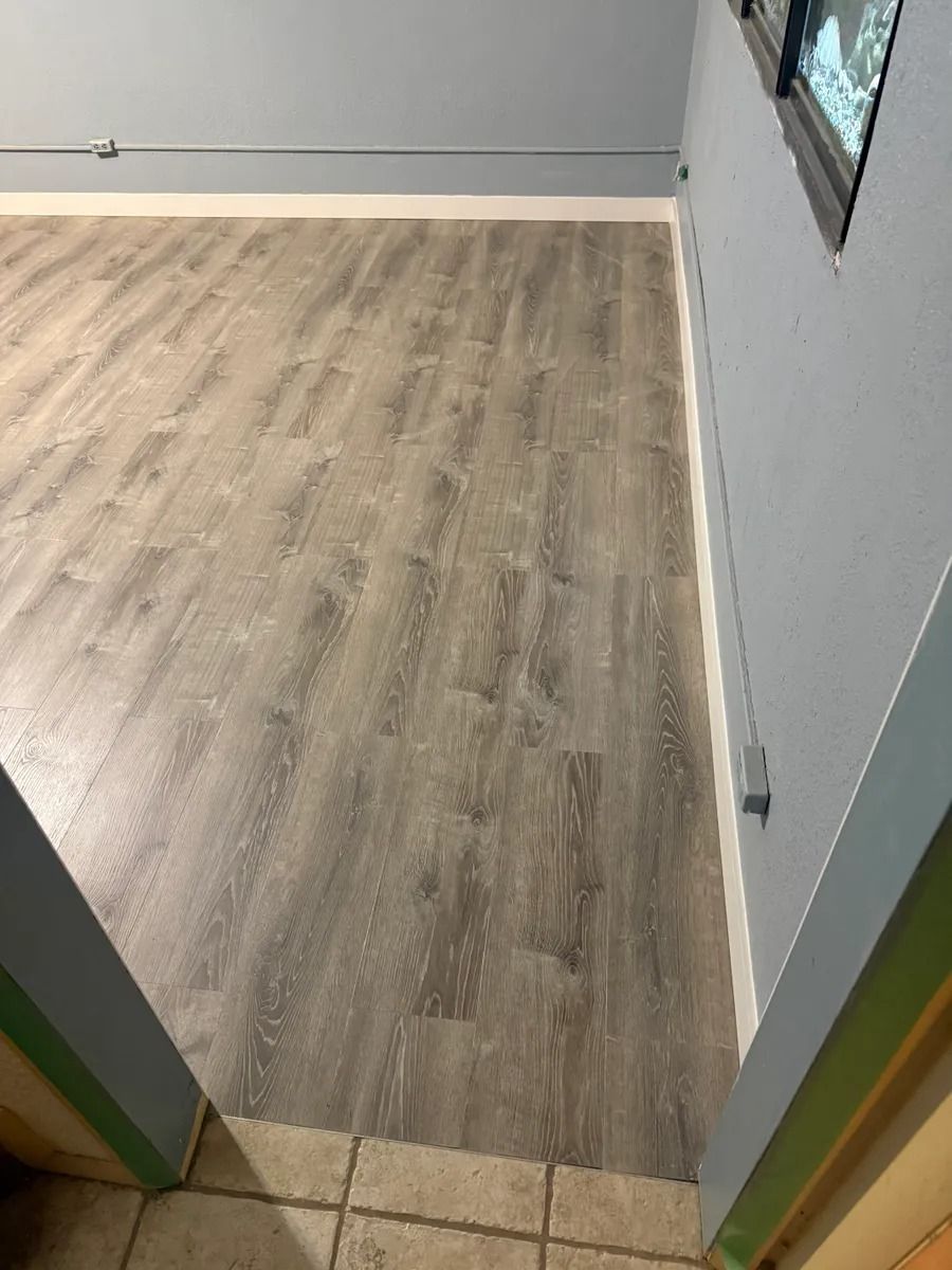 Empty room with light wood flooring, white walls, and tiled entryway at the bottom.