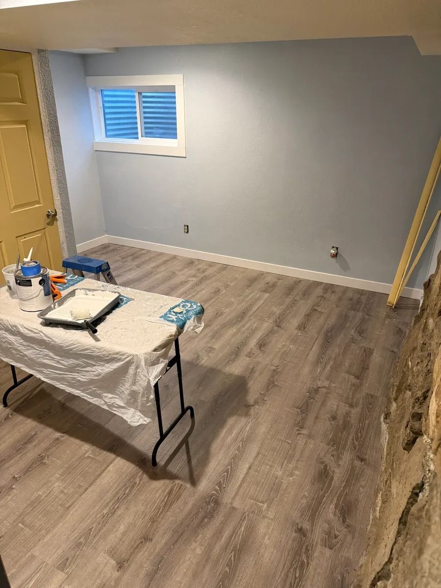 Empty room with gray walls, wood flooring, and a work table covered in painting supplies.
