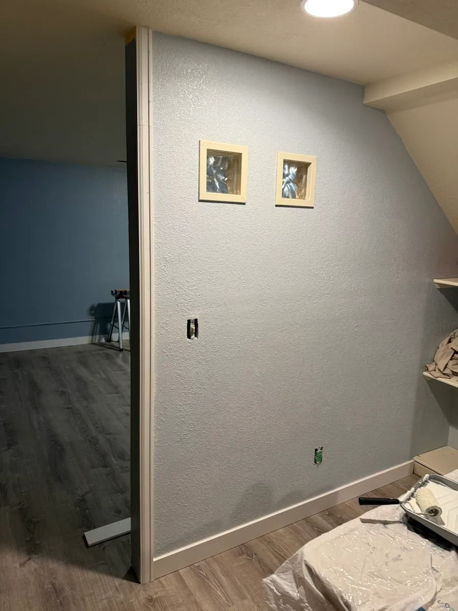 Empty room with gray walls, two small framed pictures, and dark flooring visible through an open doorway.