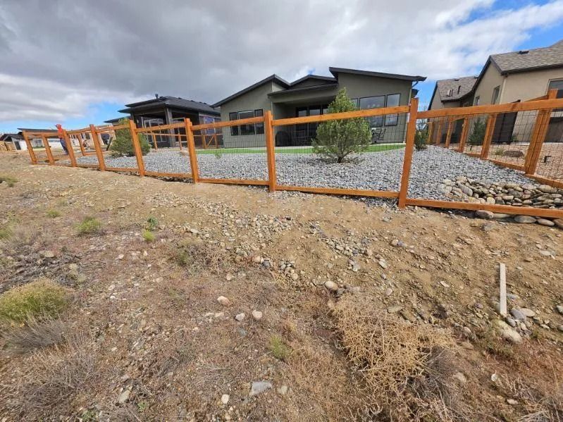 Orange construction fence around a gravel lot beside modern houses under a cloudy sky