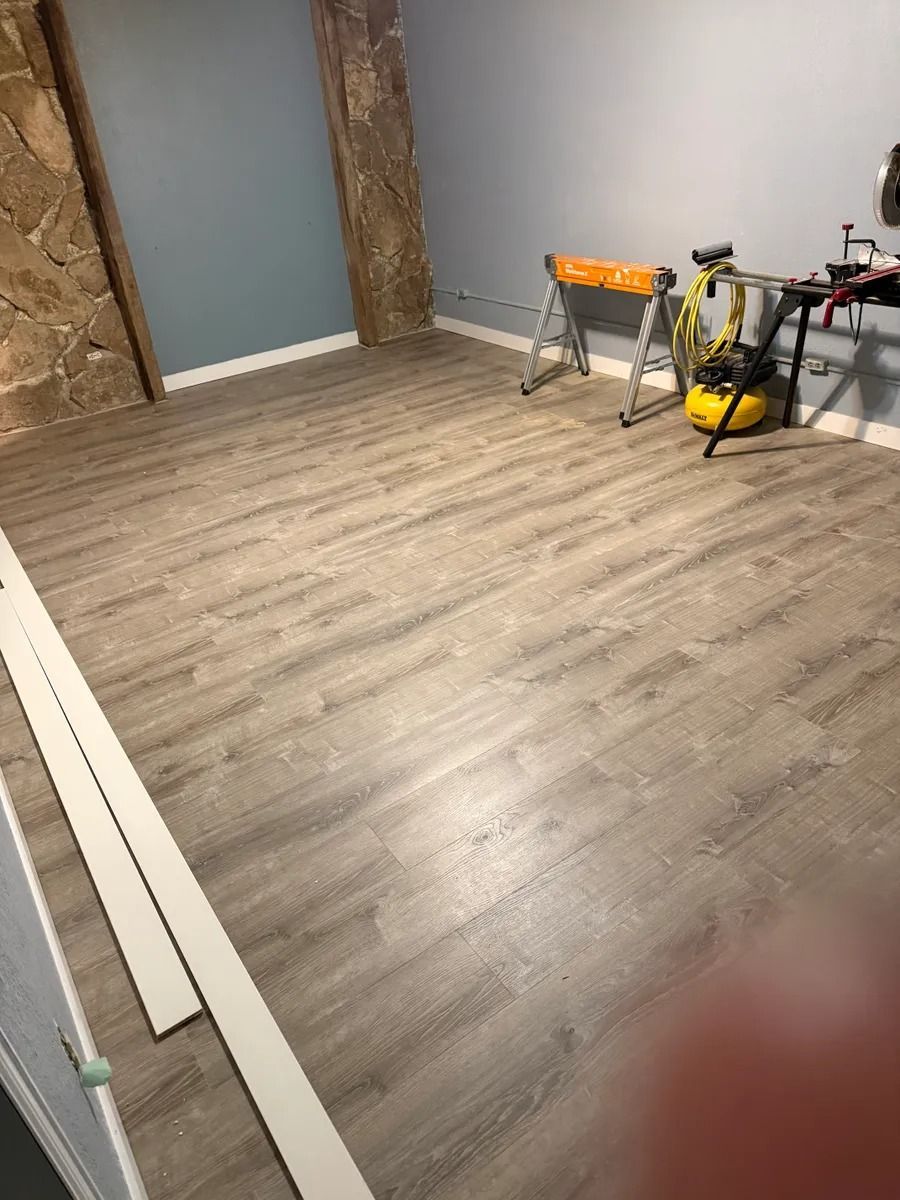 Renovated room with gray wood flooring, exposed beams, and tools near a workbench