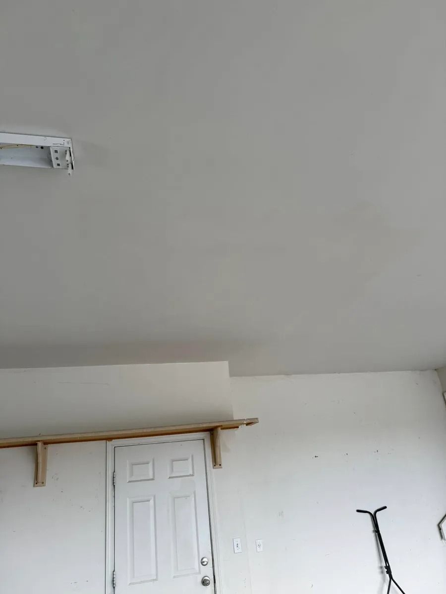 White room with a closed door, wall-mounted shelf, and part of a bicycle handlebar visible on the right.