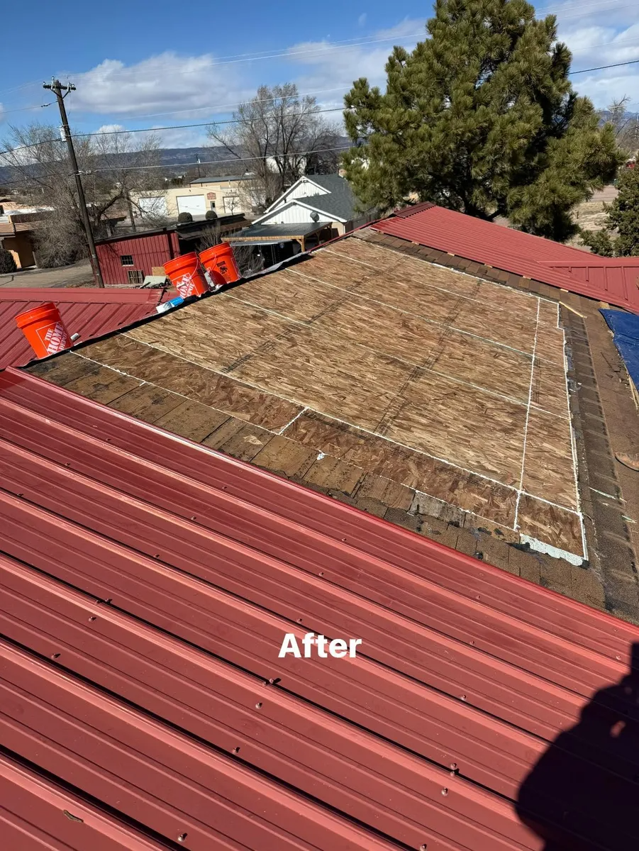 Rooftop with red metal panels and a patched brown roof section after repairs, under a blue sky.
