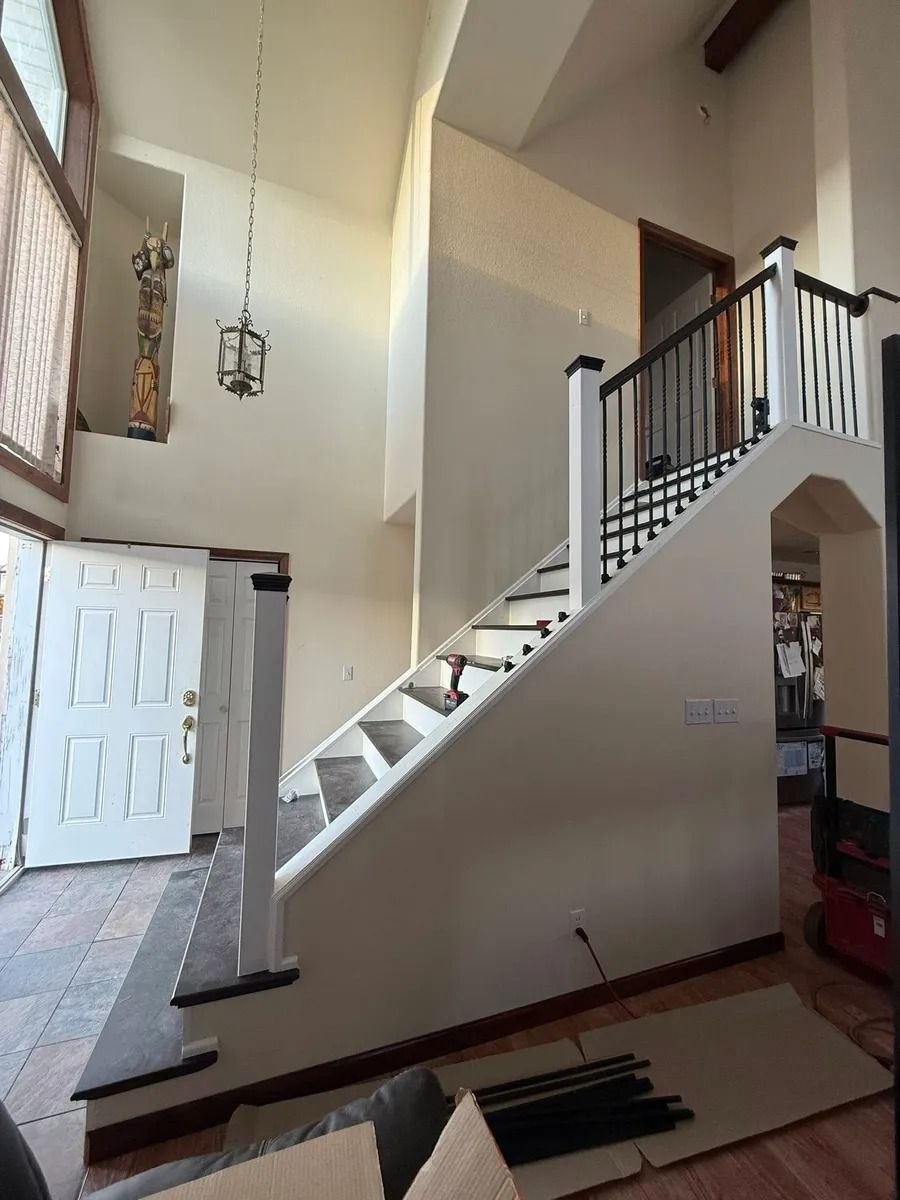 Staircase with white walls, black railing, and a hanging light in a high-ceiling entry hall
