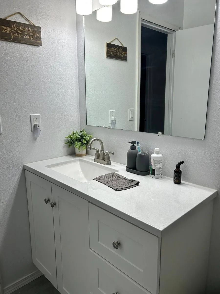 Modern white bathroom vanity with large mirror, sink, soap dispensers, and small plant on the countertop